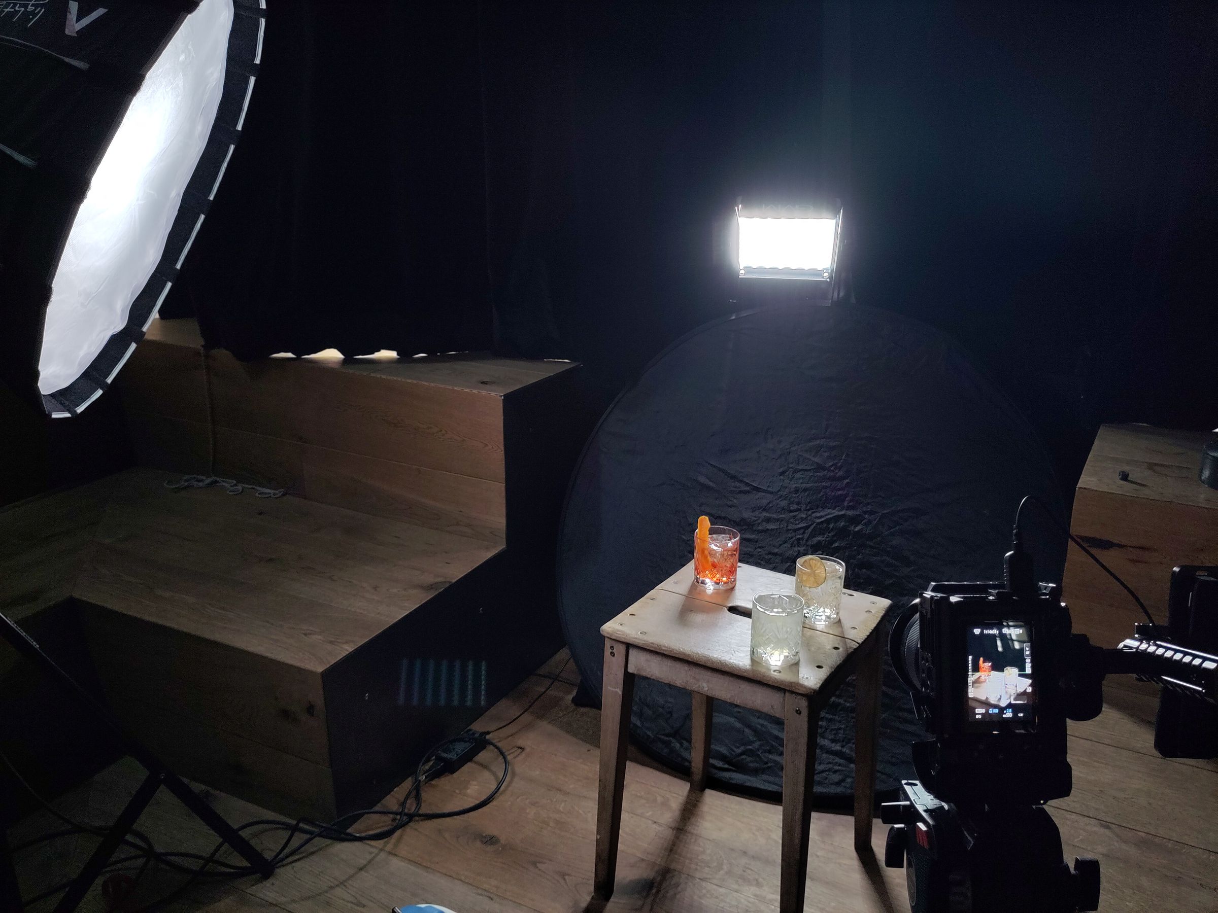 Interview-Set mit Holzpodest, Tisch, Softbox und Kamera vor schwarzem Hintergrund