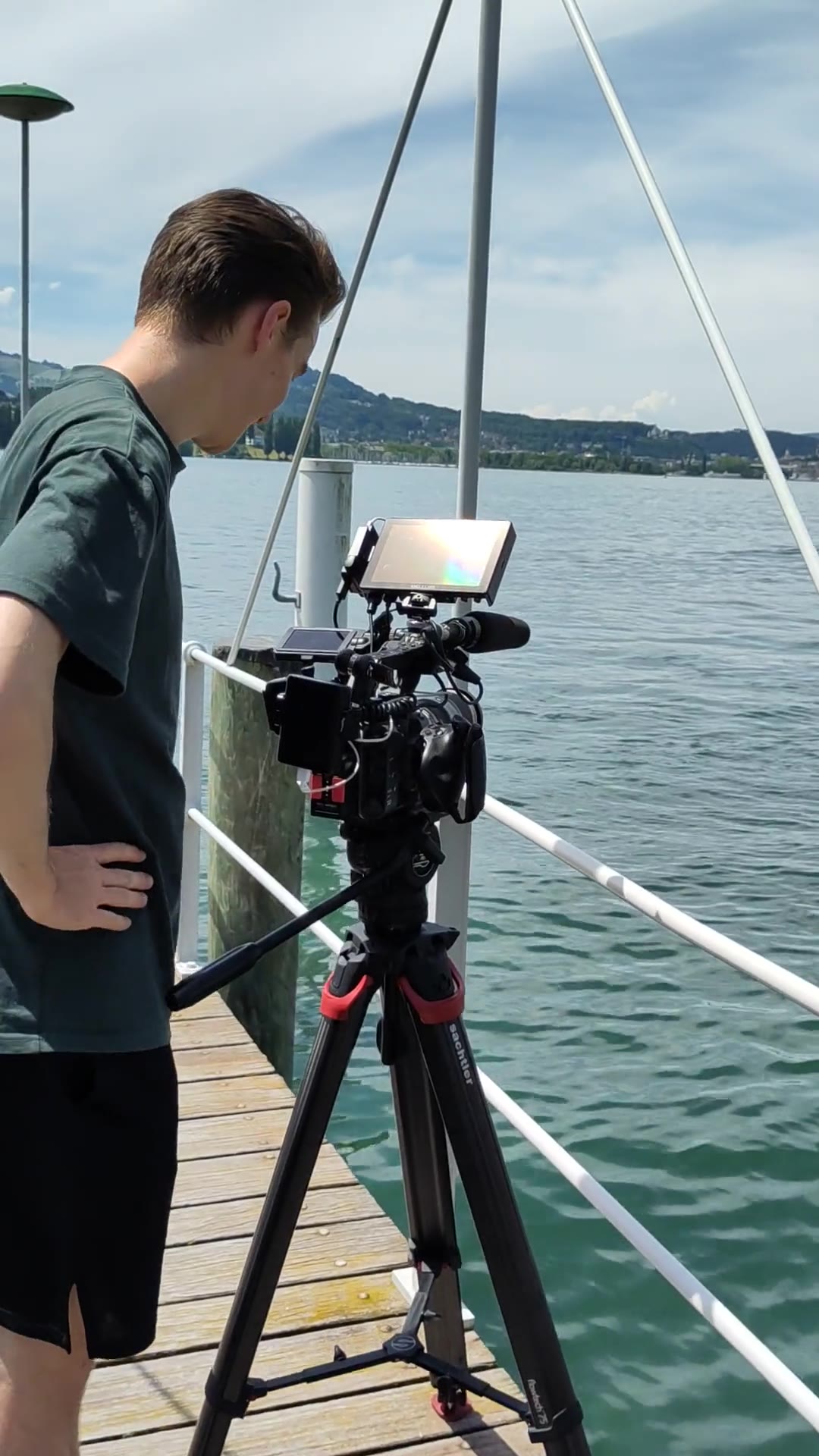 Kameramann mit Kamera auf Stativ auf einem Bootssteg am See