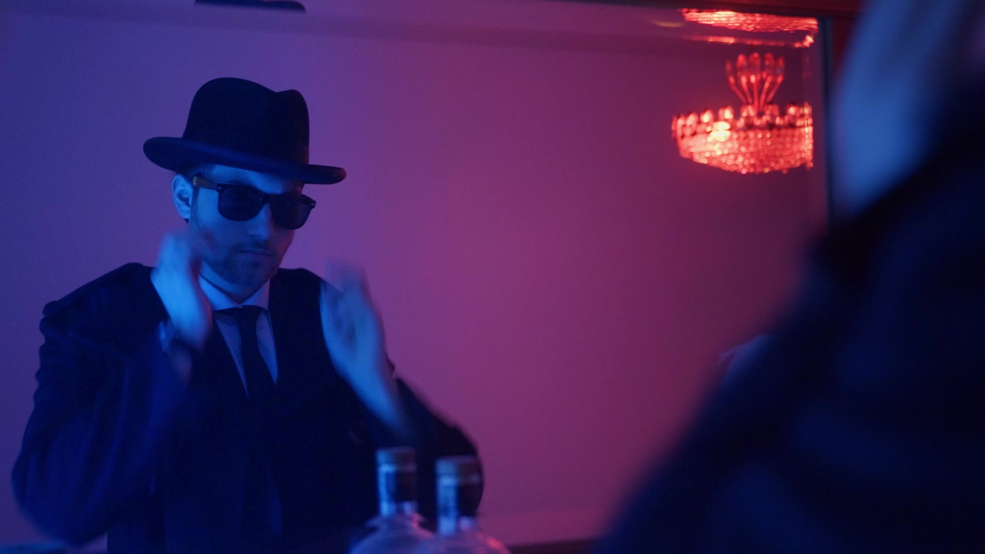 Ein Mann mit Hut und Sonnenbrille im violett-roten Licht einer Bar