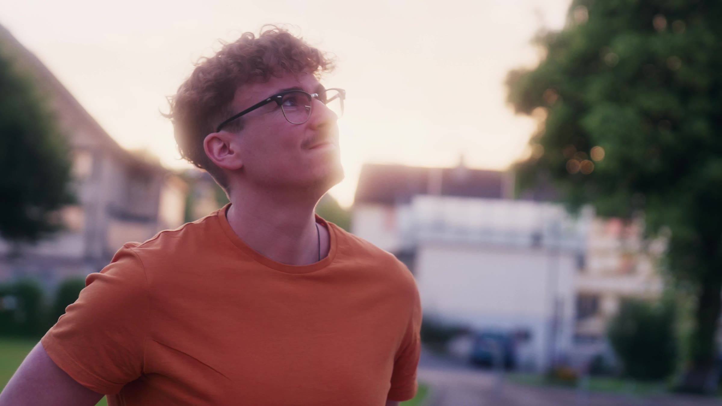 Adrian im orangen T-Shirt blickt im Abendlicht nach oben