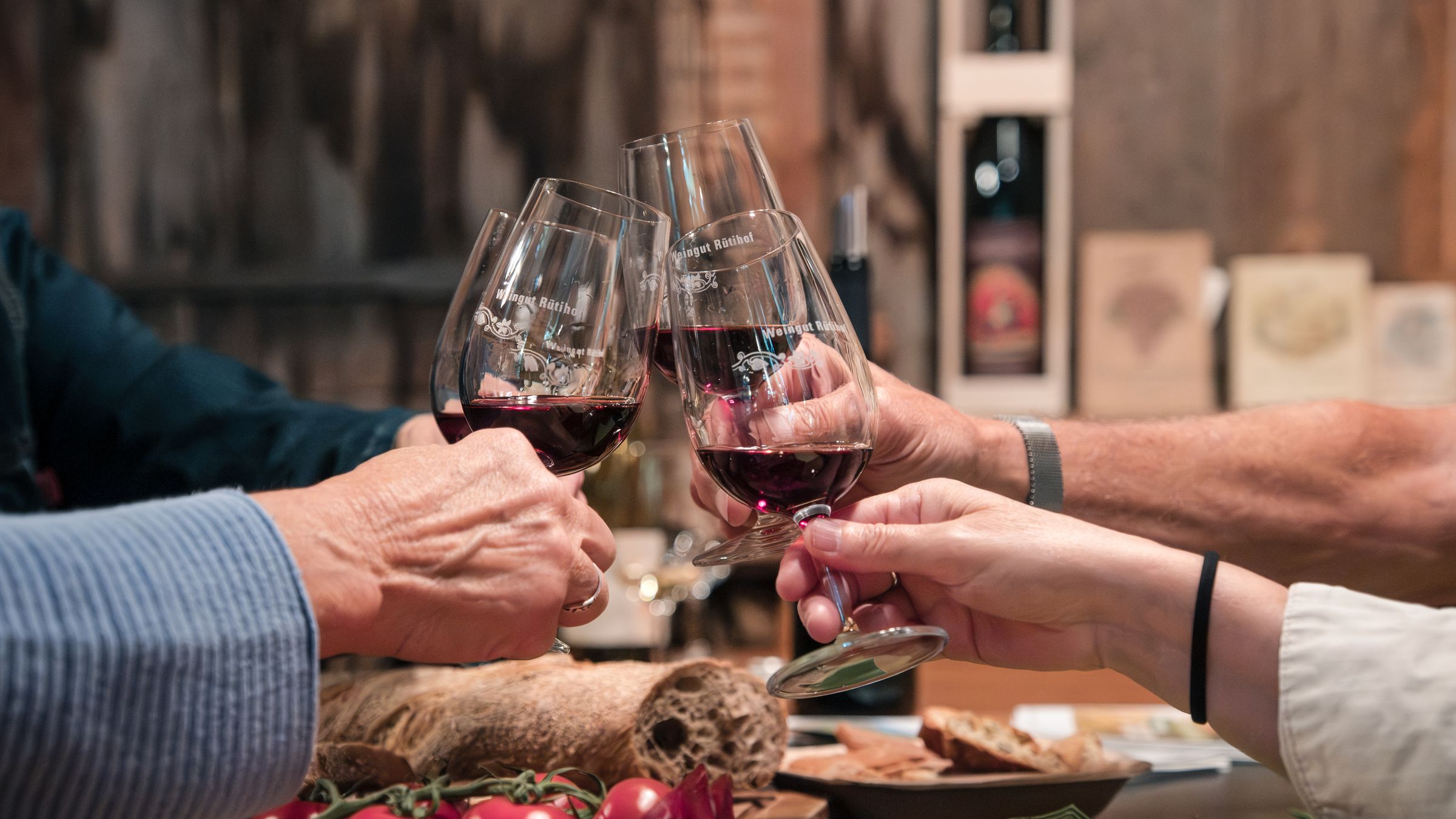 Gäste stossen an der Degustation im Weingut Rütihof mit Rotwein an, davor ein Plättli mit Käse, Trockenfleisch und Tomaten