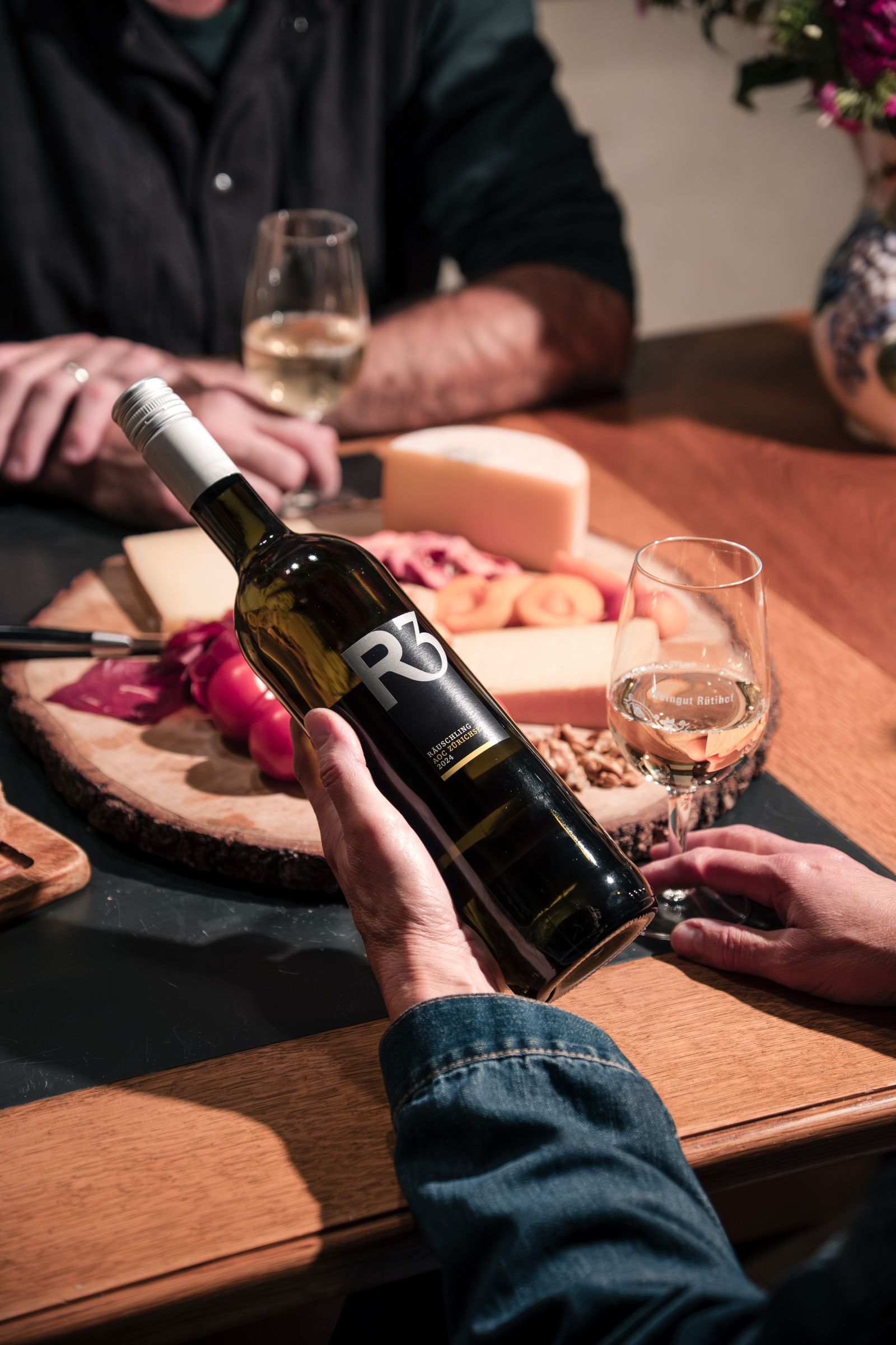 Flasche R3 Räuschling vom Weingut Rütihof in der Hand, im Hintergrund ein Plättli