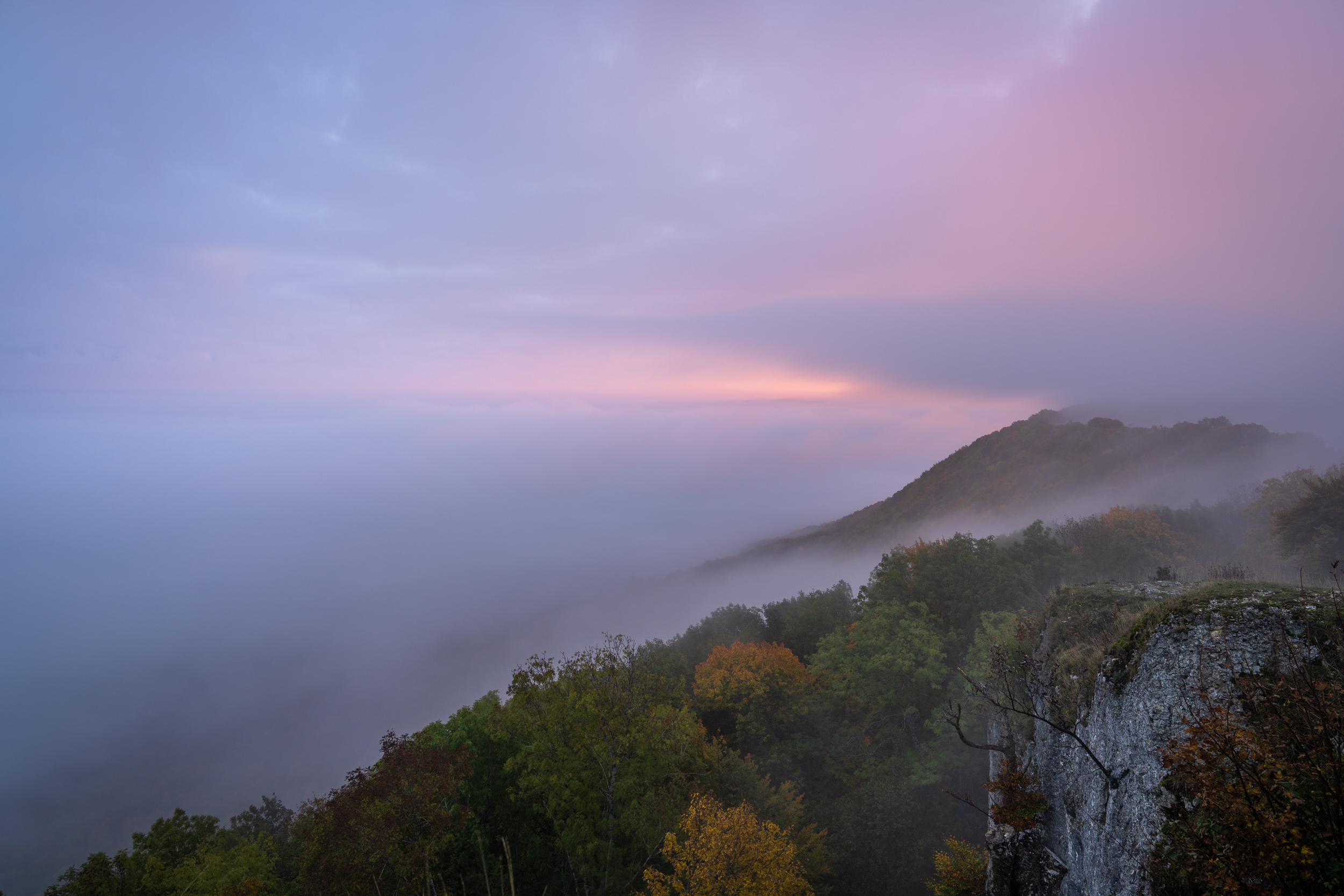 Nebelmeer an der Albkante, Felsen und Herbstwald im rosa Morgenlicht
