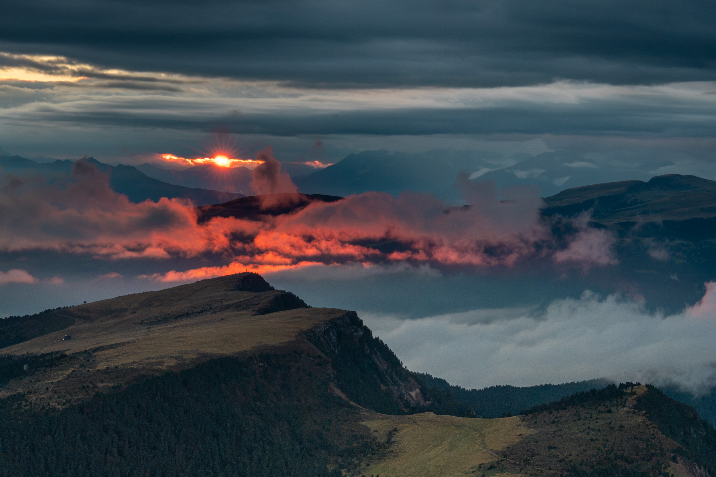 Sonnenuntergang zwischen Wolkenschichten über Bergkämmen und Nebelfeldern