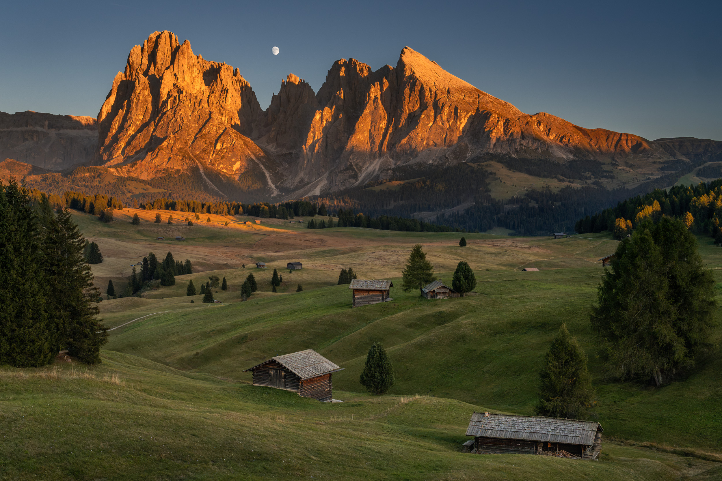 Almhütten auf der Seiser Alm, dahinter Lang- und Plattkofel im Abendlicht und der Mond
