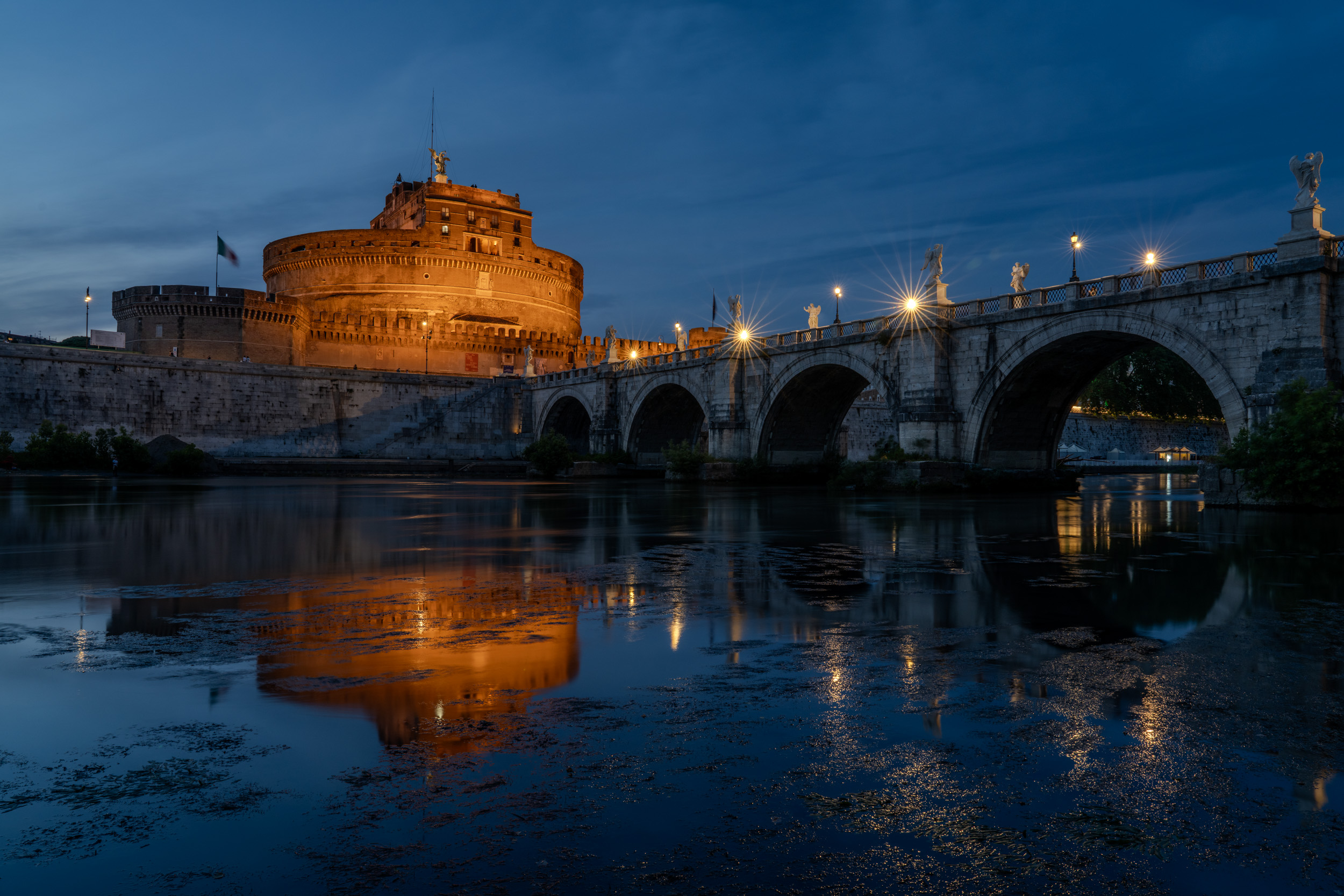Engelsburg und Engelsbrücke zur blauen Stunde, die Lichter spiegeln sich im Tiber