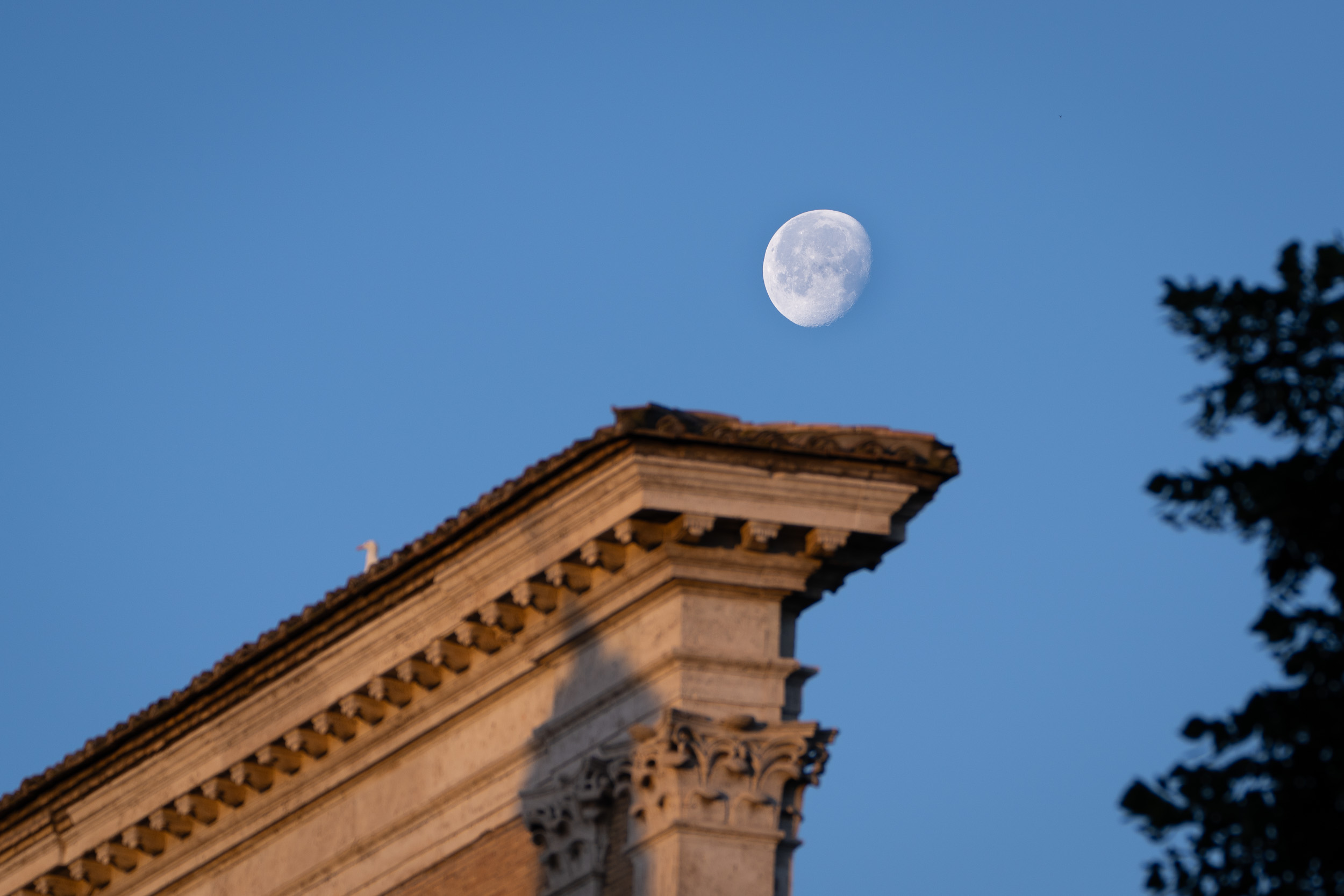 Der Mond über dem Giebel eines Gebäudes im ersten Morgenlicht