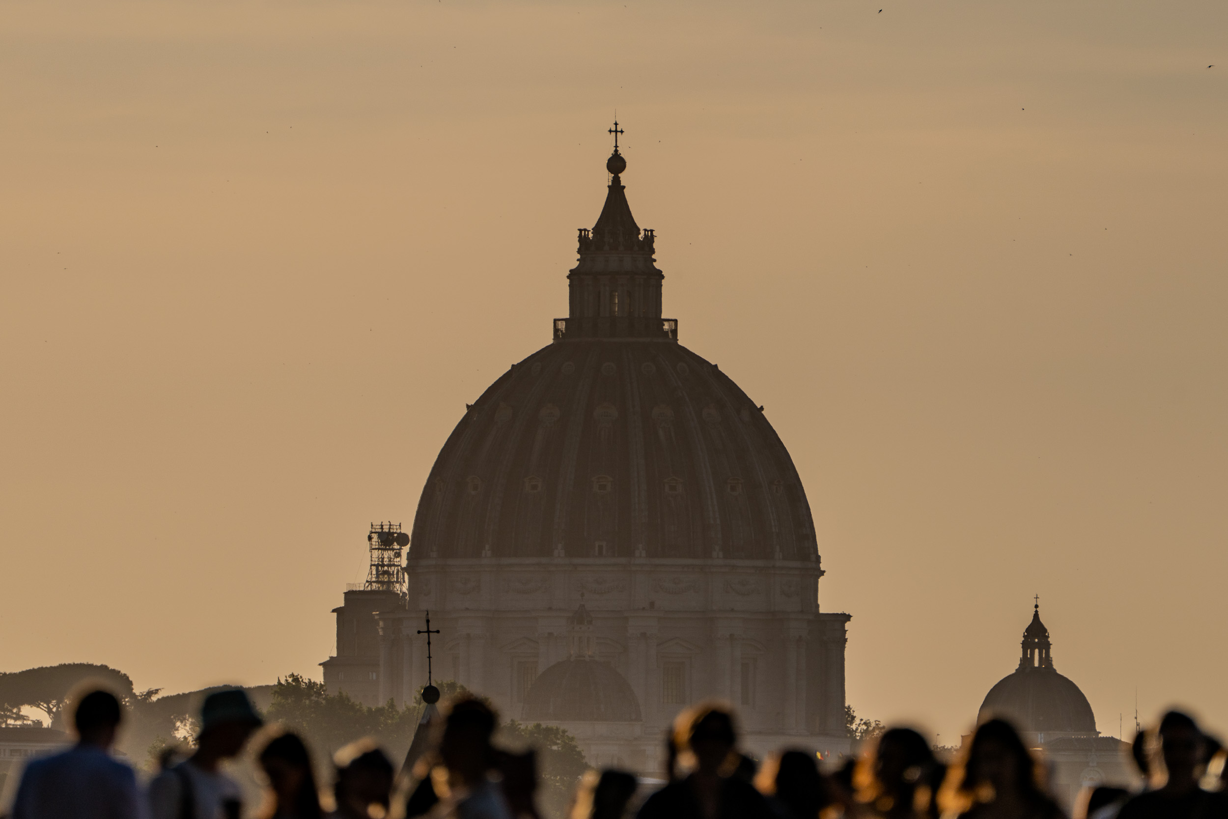 Silhouette der Petersdom-Kuppel im Abenddunst, im Vordergrund Menschen als Schattenrisse