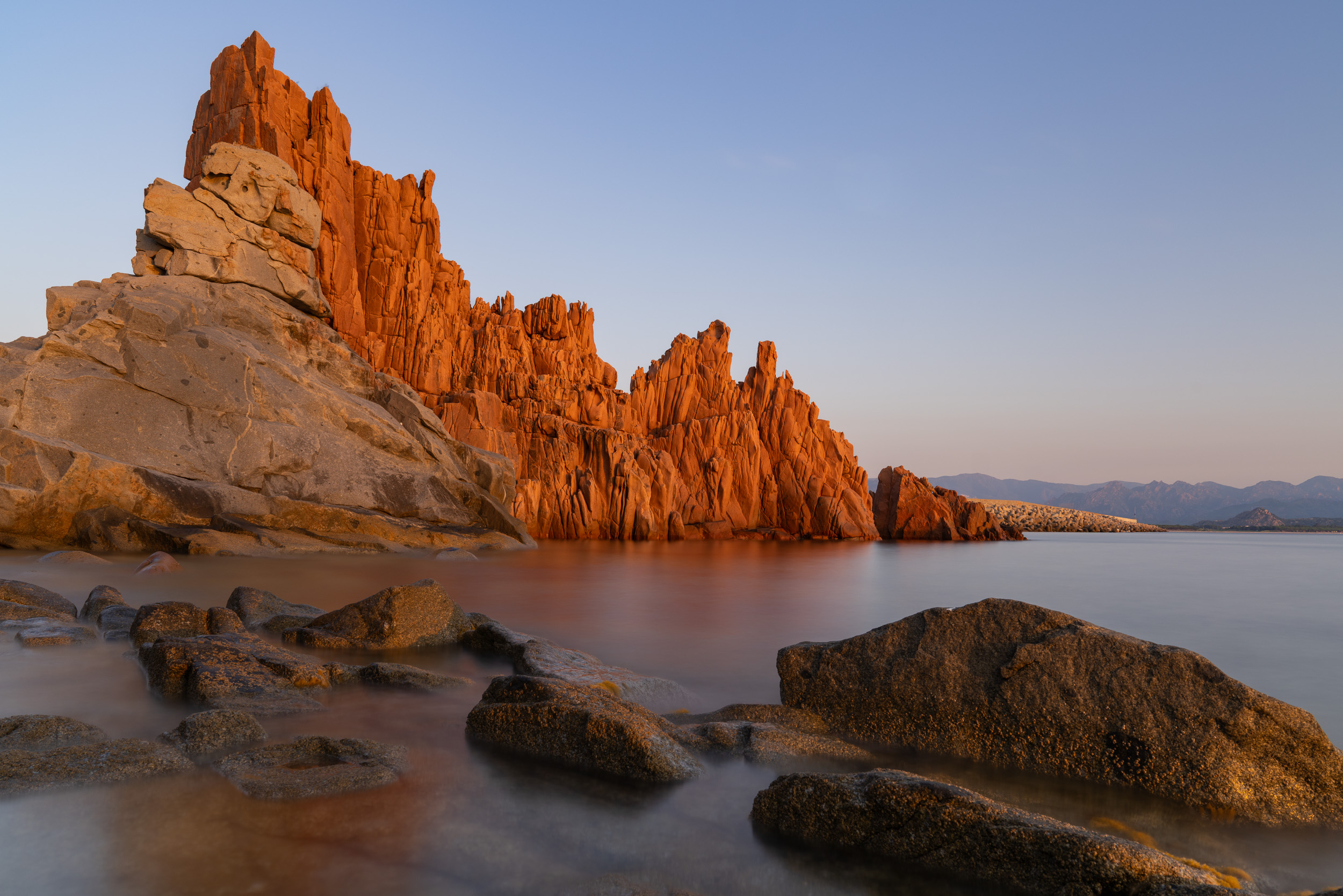 Rote Porphyrfelsen der Rocce Rosse leuchten im Morgenlicht über dem Meer