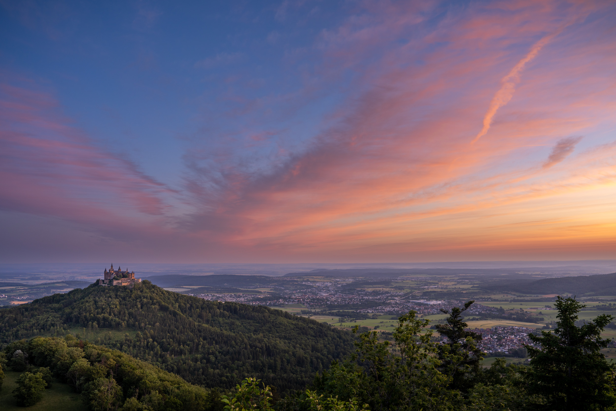 Burg Hohenzollern unter leuchtend rosa Wolken bei Sonnenaufgang, davor das Albvorland