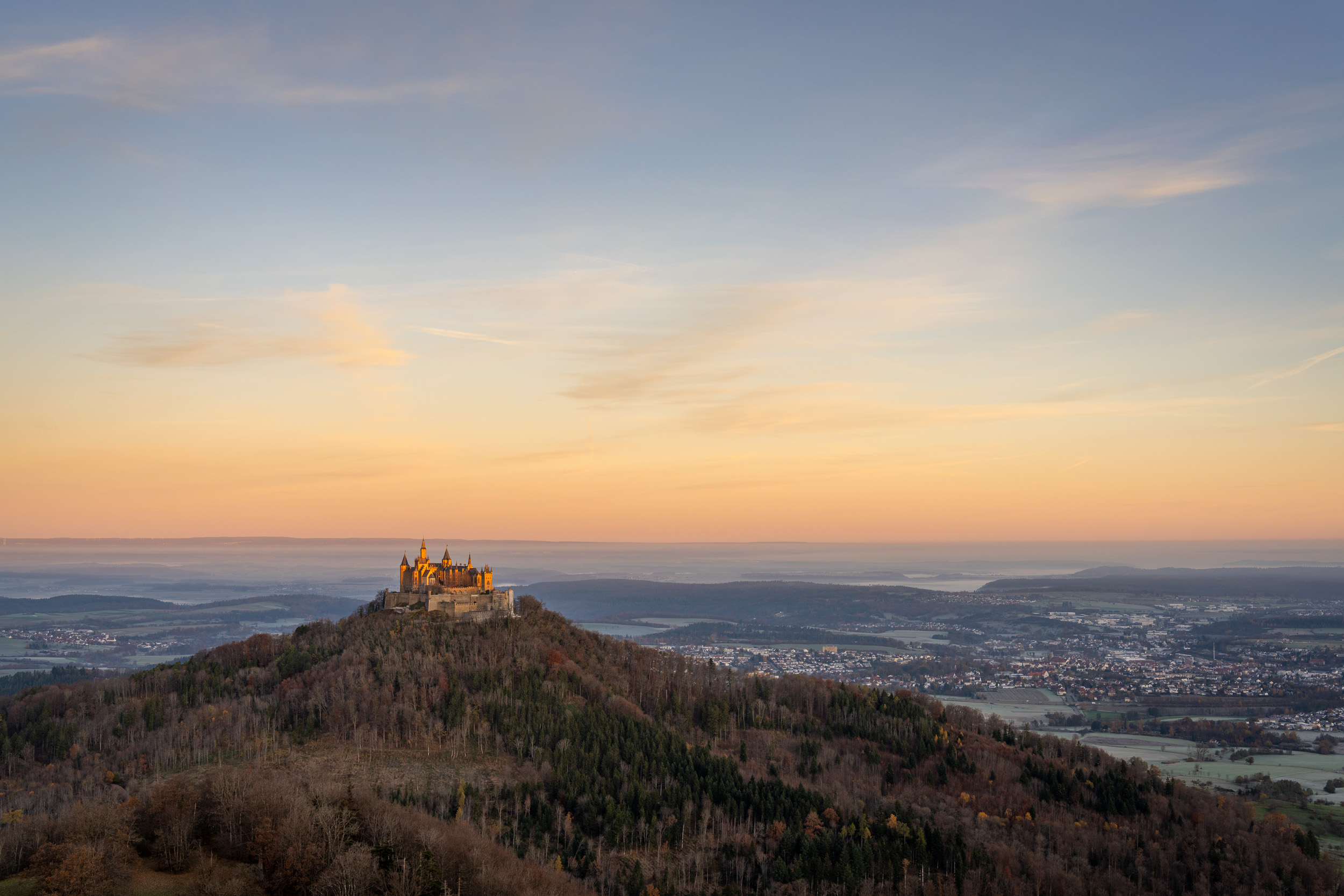 Burg Hohenzollern im goldenen Morgenlicht, dahinter das weite Albvorland