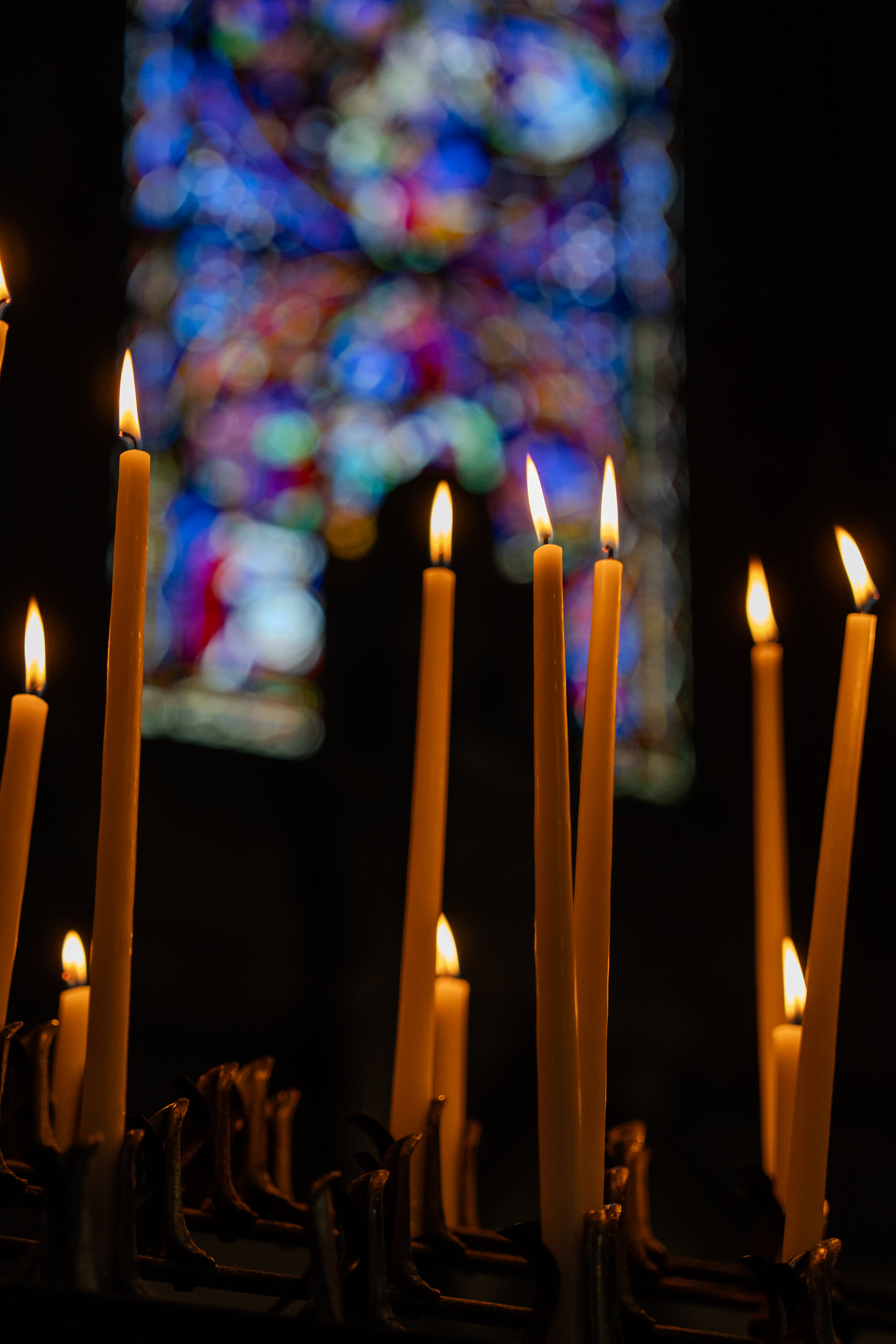 Brennende Kerzen vor einem bunten Kirchenfenster