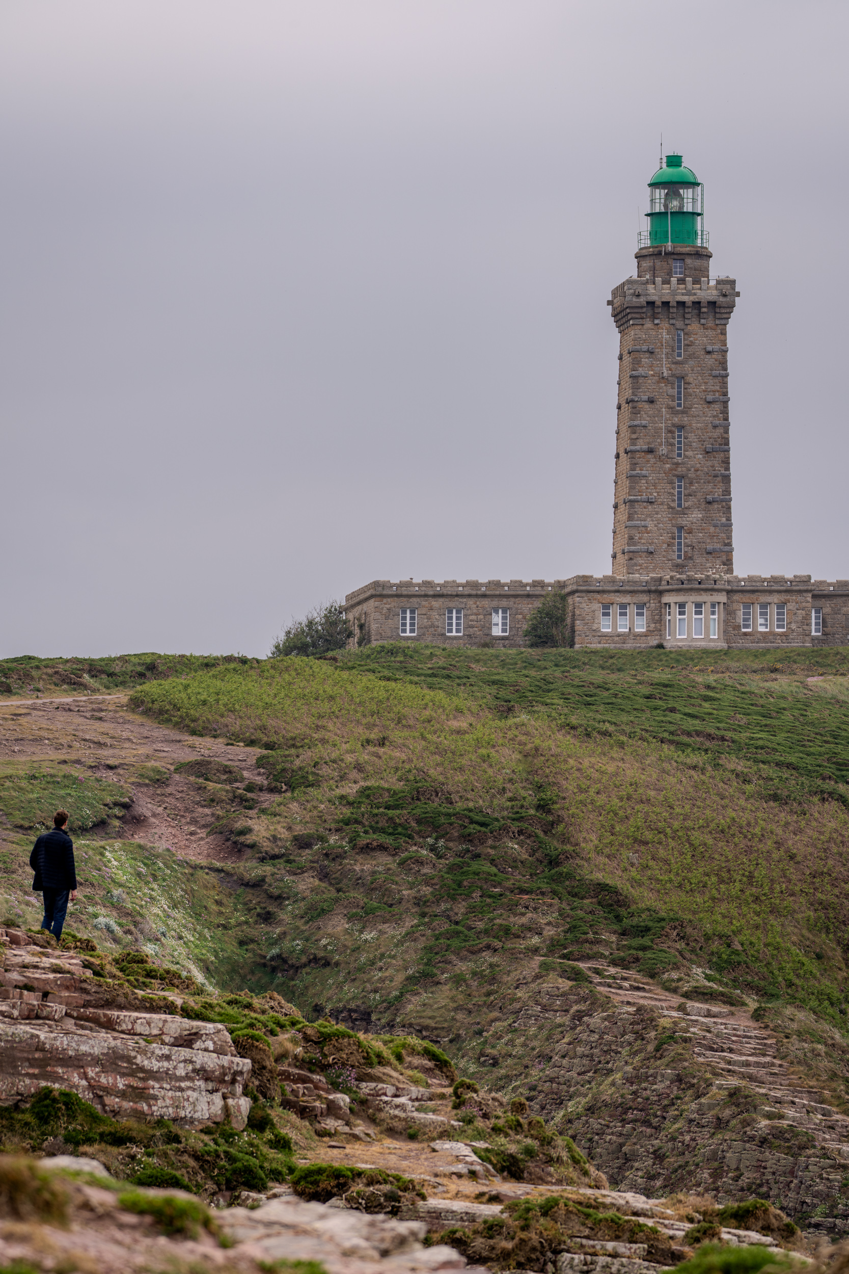 Person auf den Klippen vor dem Leuchtturm am Cap Fréhel