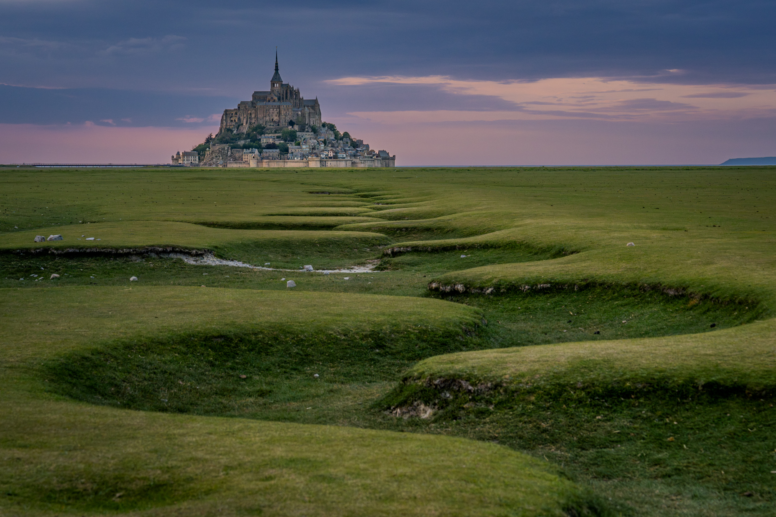 Mont-Saint-Michel in der Abenddämmerung, davor Salzwiesen mit Prielen