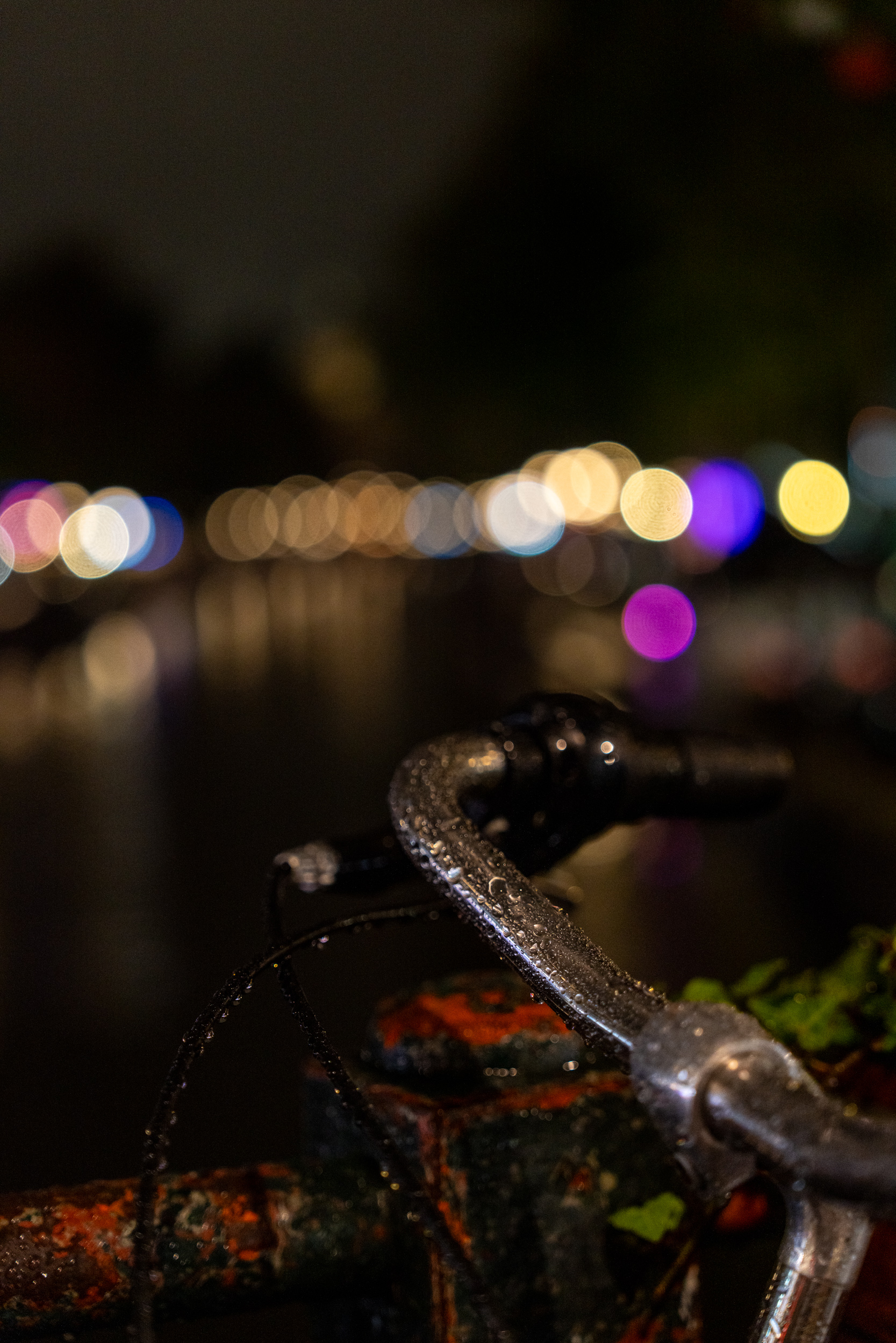 Nasser Fahrradlenker vor den unscharfen Lichtern einer Gracht