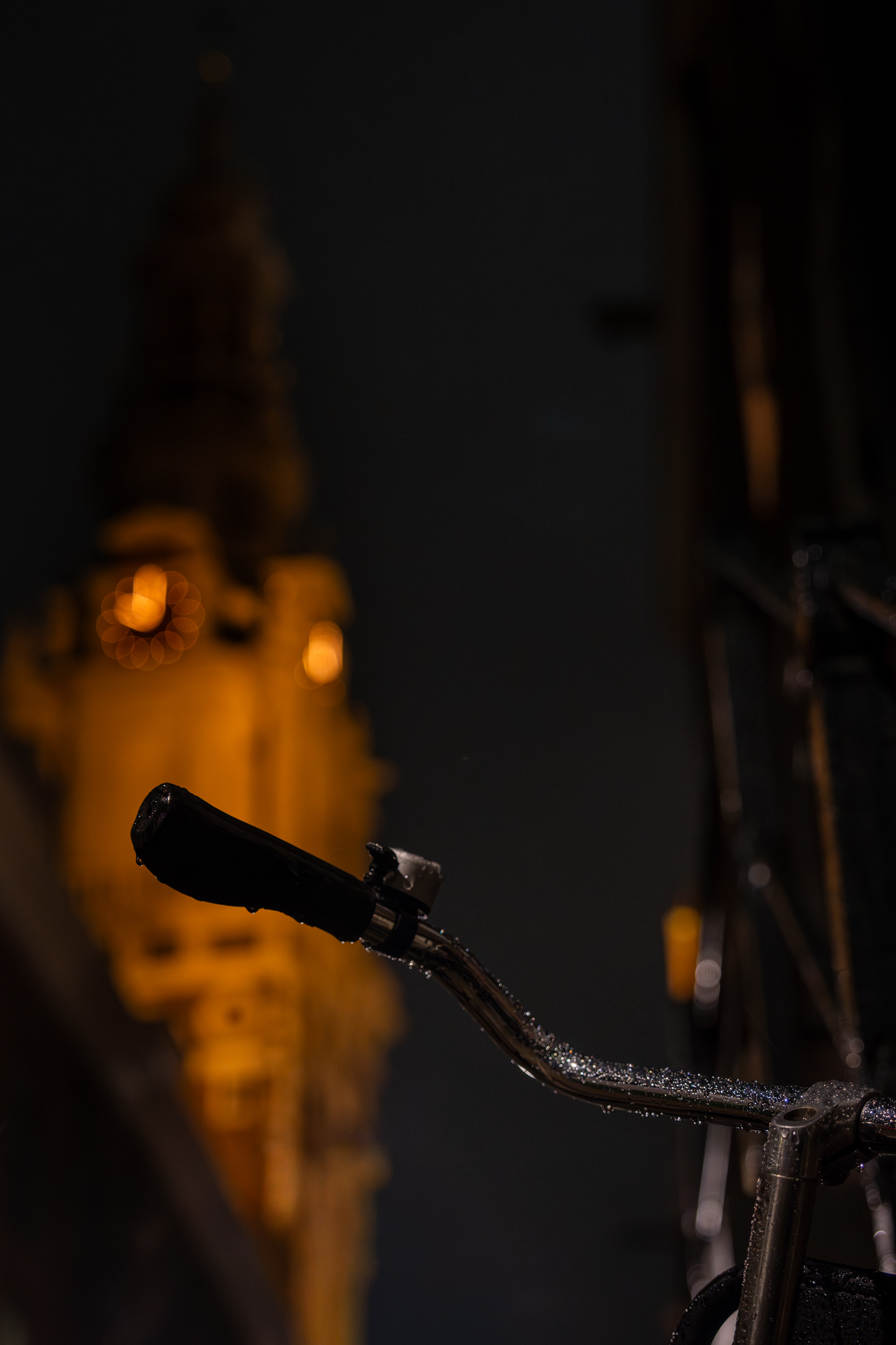 Fahrradlenker mit Regentropfen, im Hintergrund unscharf die beleuchtete Zuiderkerk