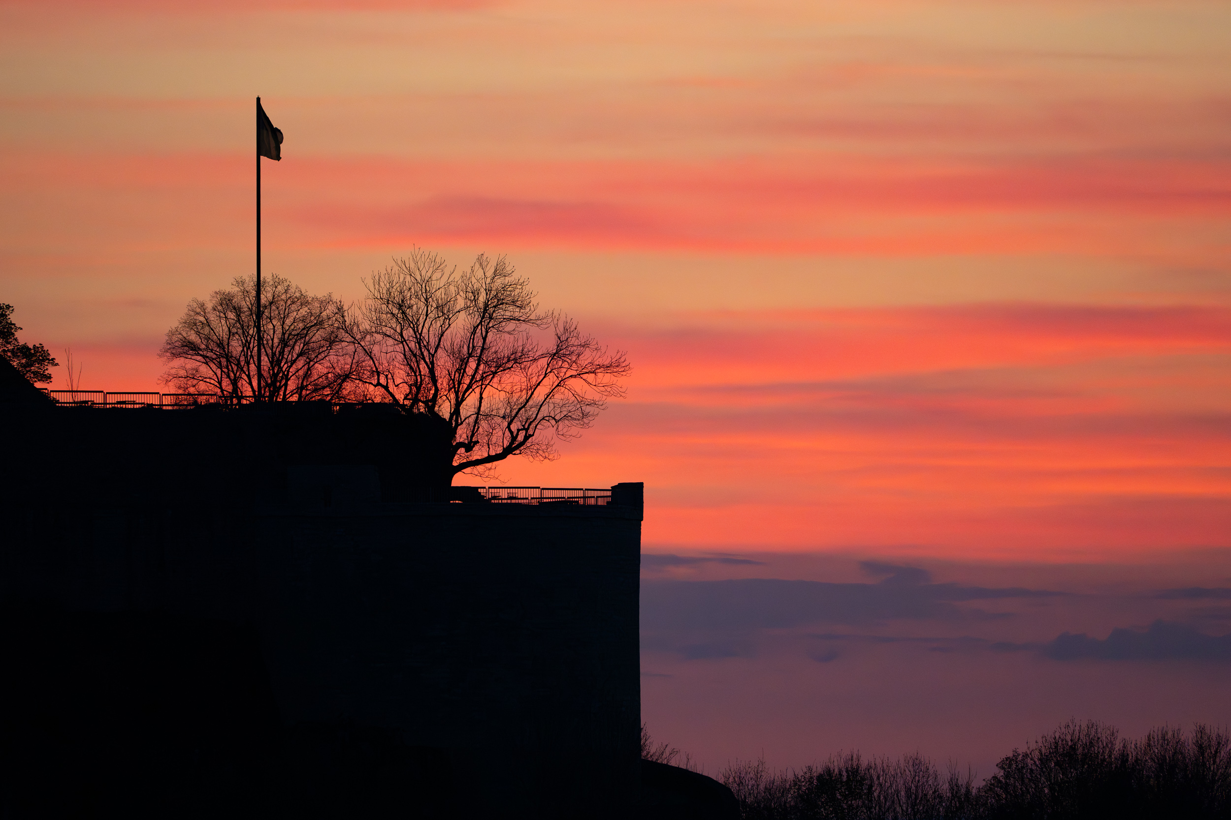 Silhouette der Burgmauern mit Fahne vor rot gestreiftem Abendhimmel