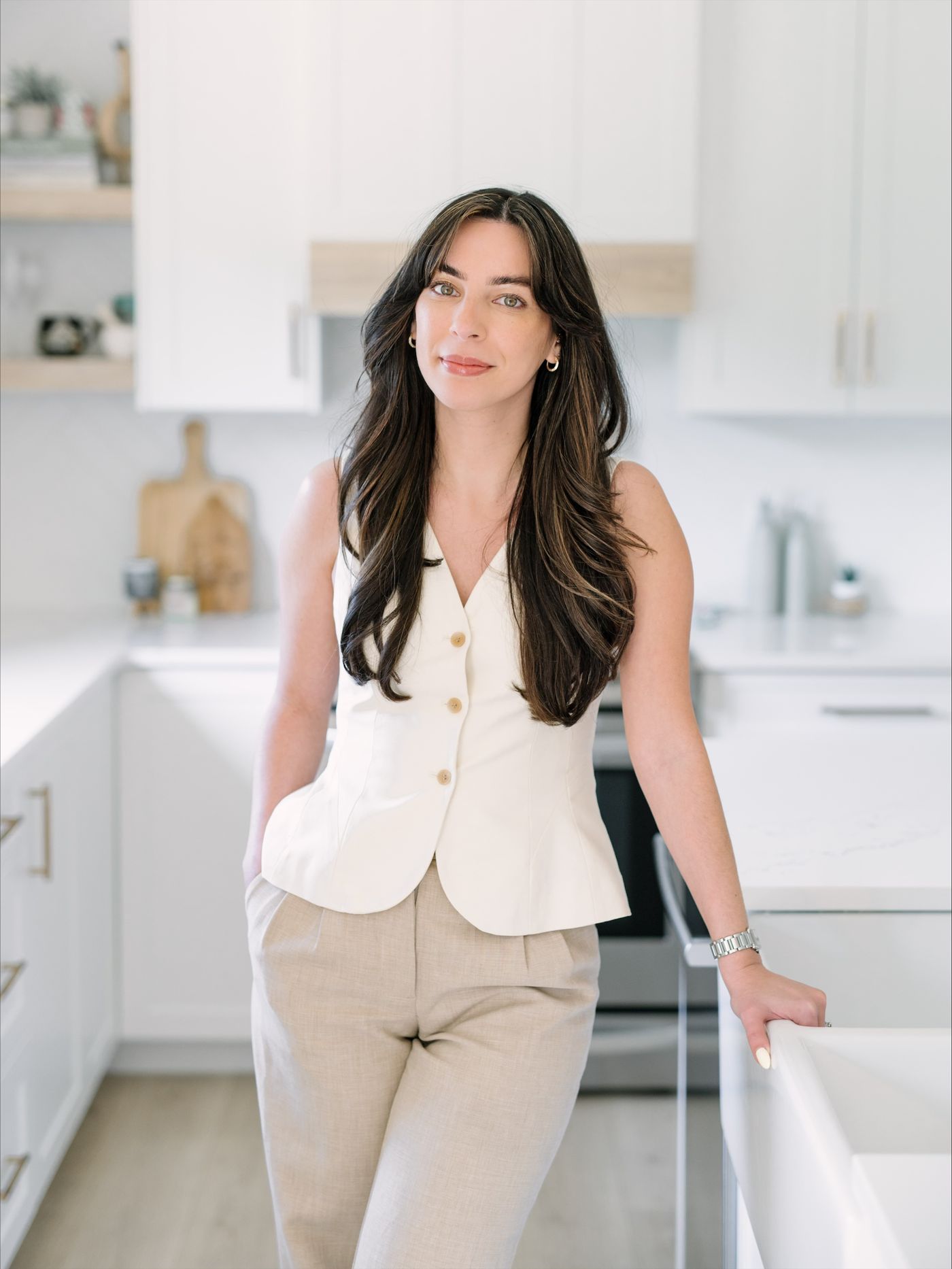 Jessica Ramia standing in a bright white kitchen, wearing a cream vest and beige trousers