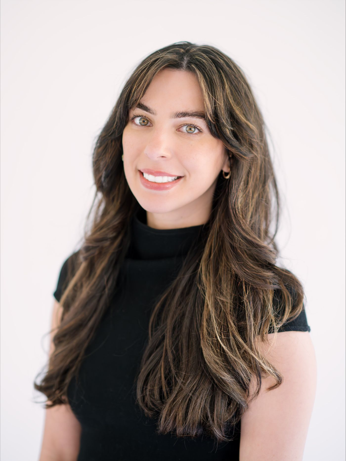 Portrait of Jessica Ramia smiling, in a black top against a white wall