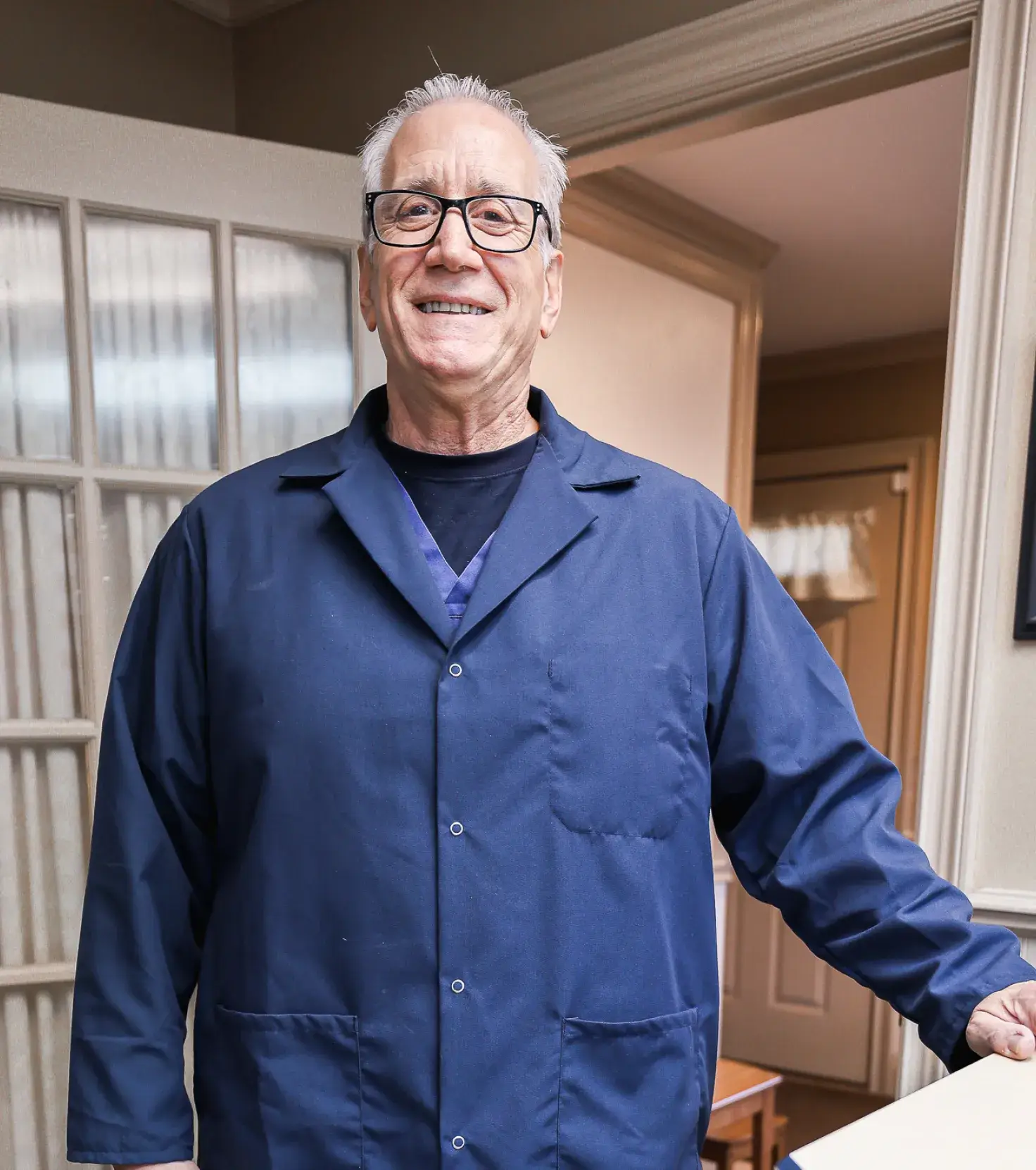A man in a blue lab coat standing in a room.