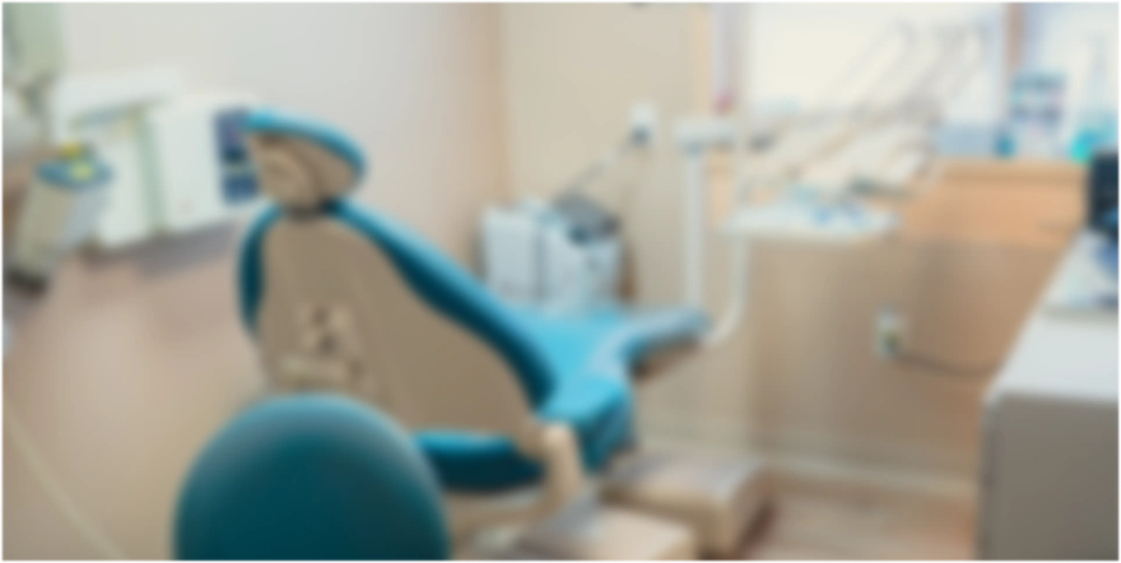 Blurred image of a dental examination room with a dental chair and equipment.