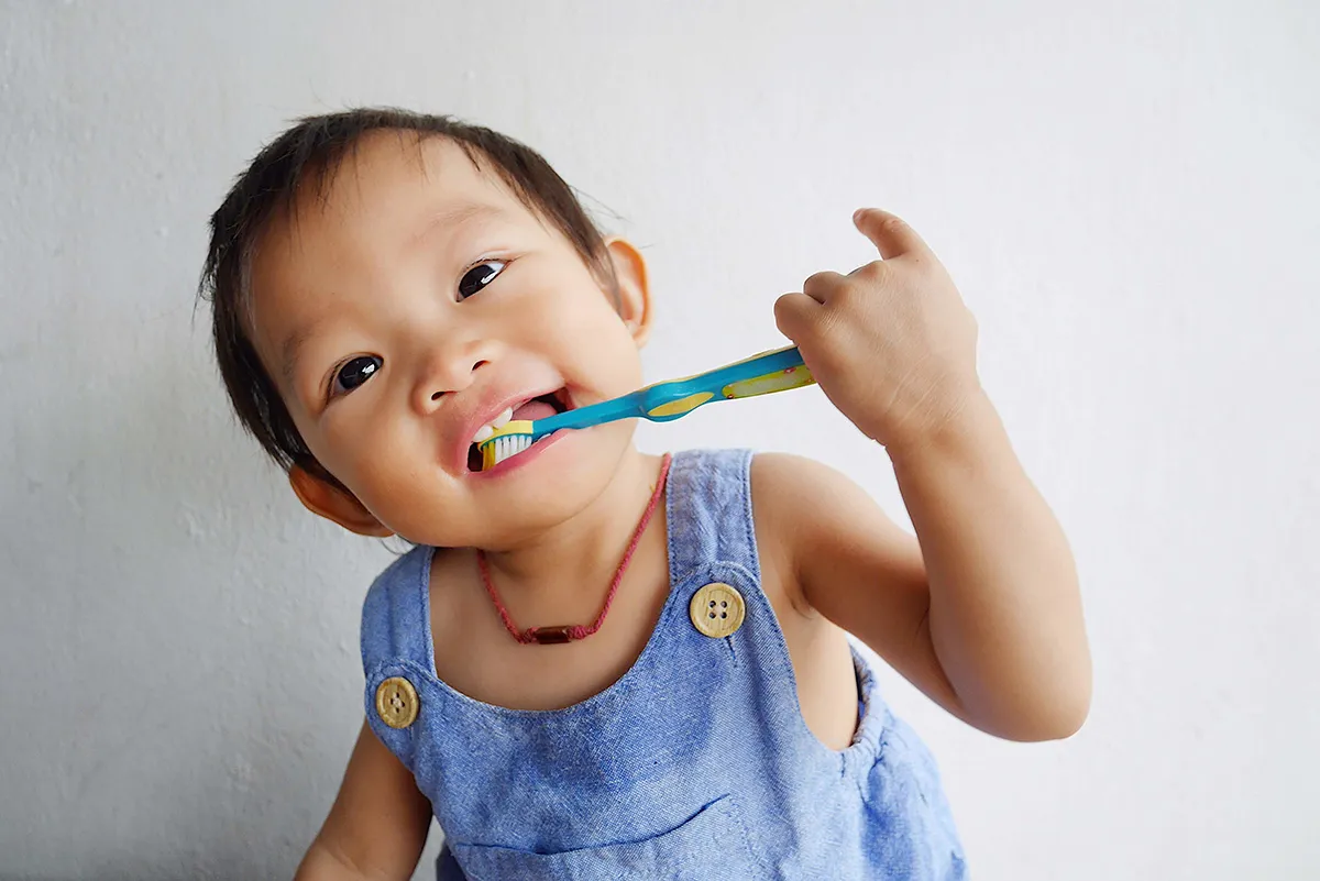 A young child enthusiastically brushes their teeth with a colorful toothbrush, dressed in a denim outfit and smiling brightly. This image captures the essence of developing healthy habits early, emphasizing the importance of pediatric oral care and encouraging independence in daily hygiene routines.