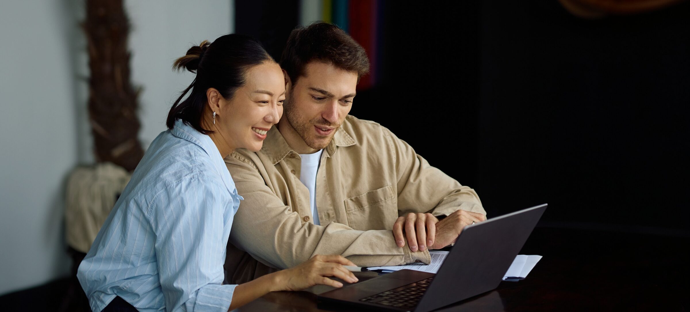 A couple smiling as they look at a laptop together