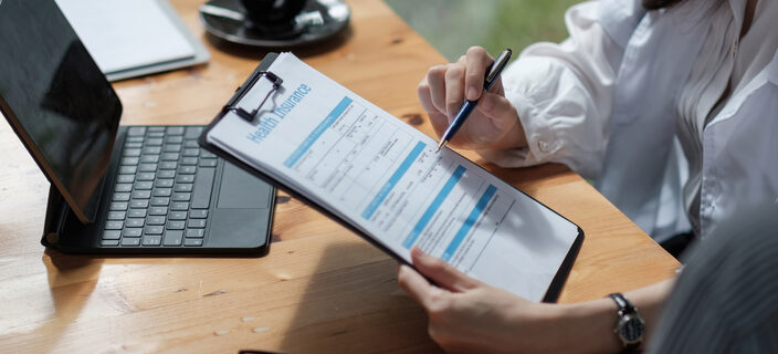 A person filling out a health insurance form on a clipboard