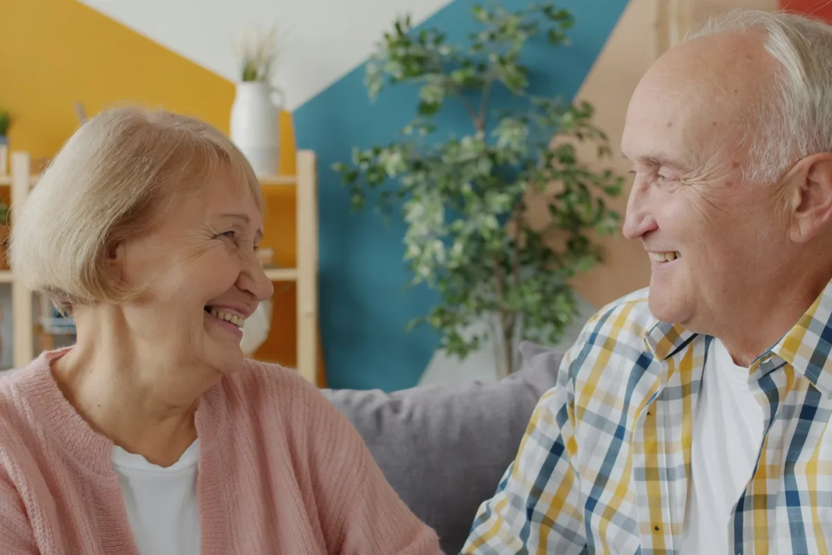 An older couple sitting on a couch and smiling at each other