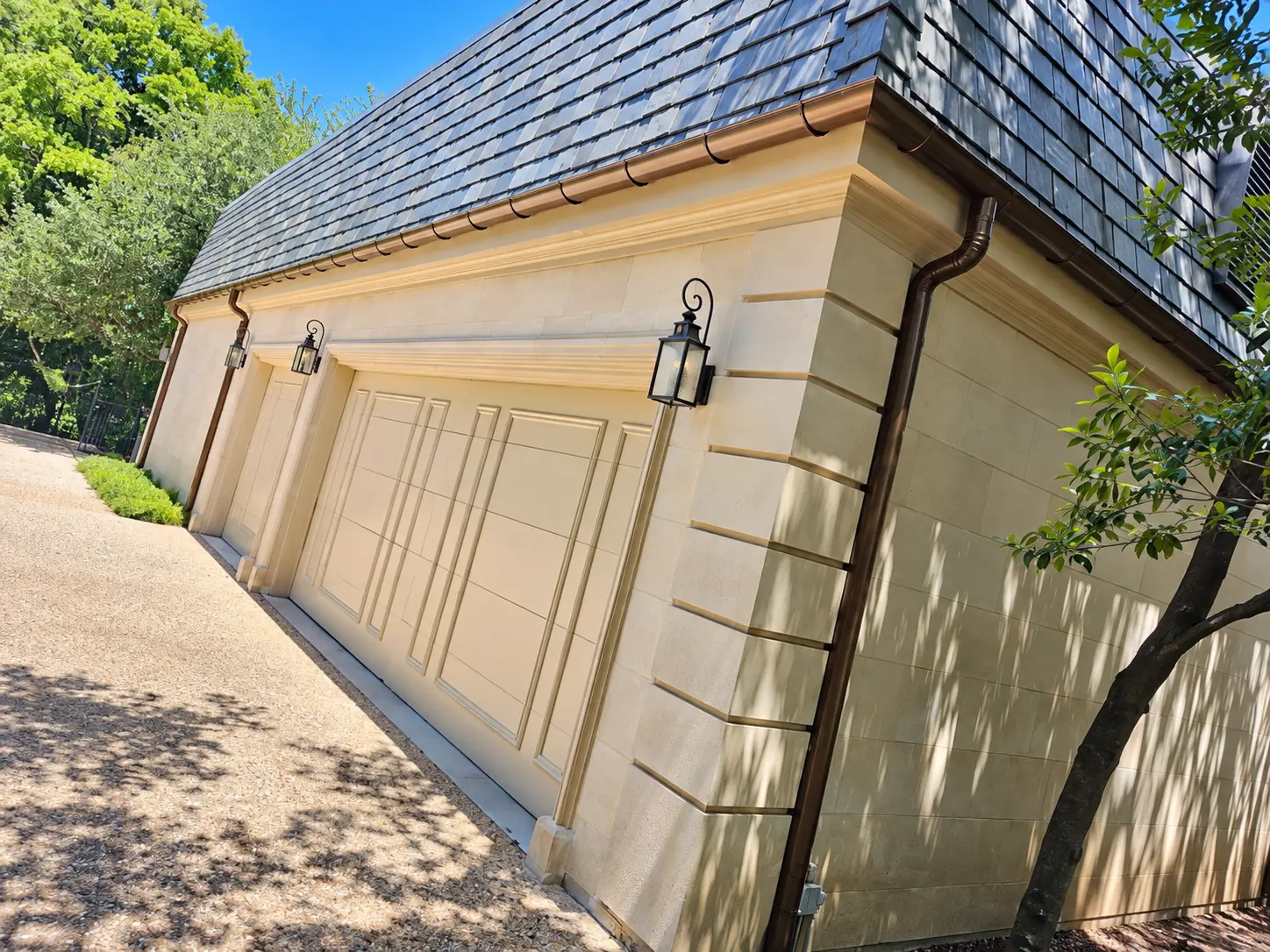 Copper-tone half-round gutters and downspout on a stone garage with a slate roof