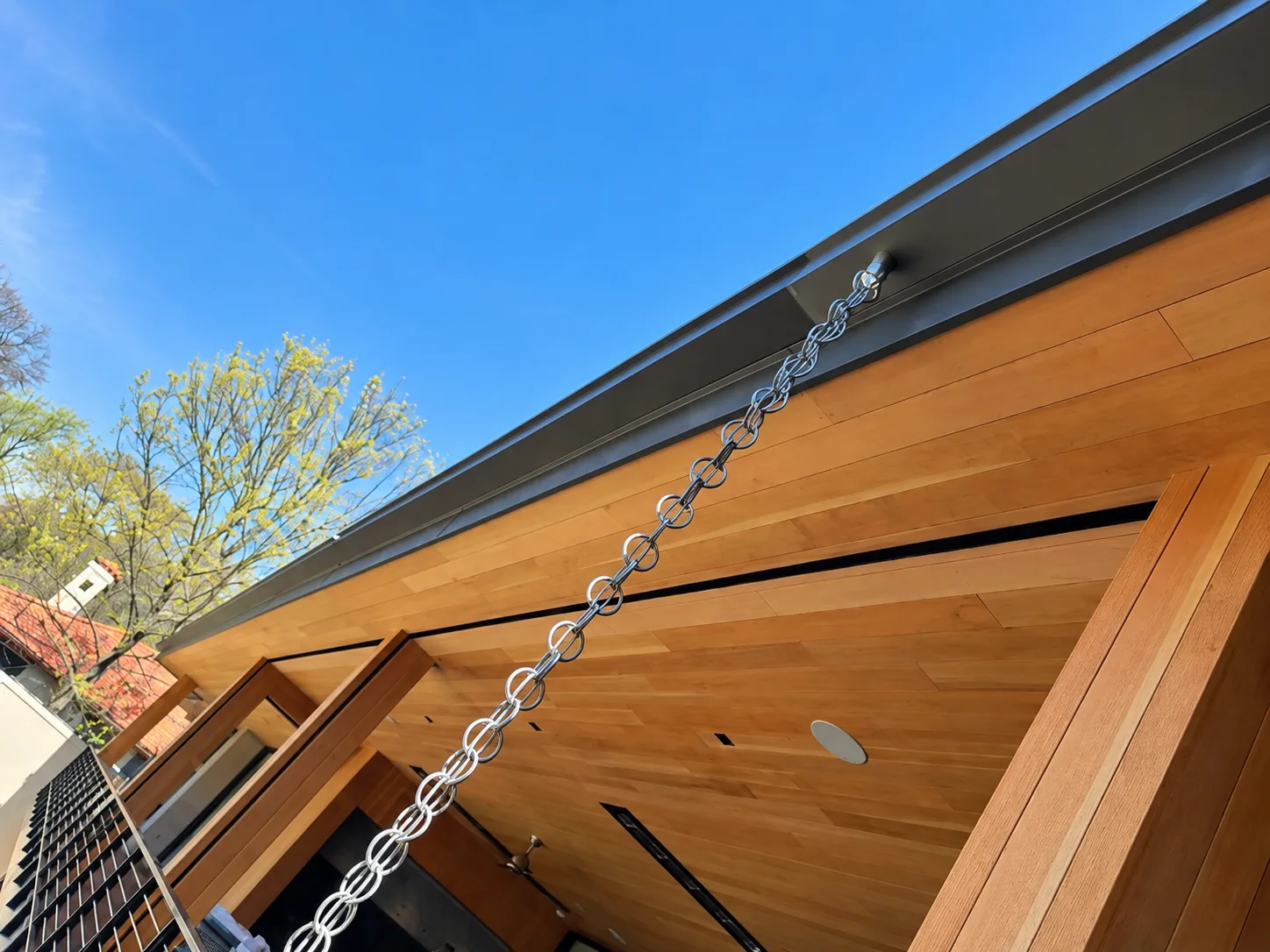 Rain chain hanging from a dark box gutter beside a stained wood soffit