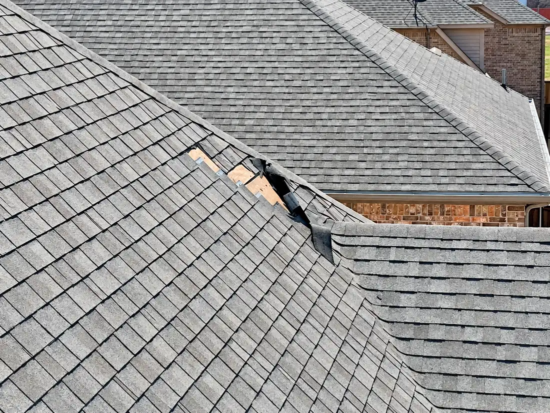 Wind-torn shingles near a hip on a shingle roof with roof decking exposed
