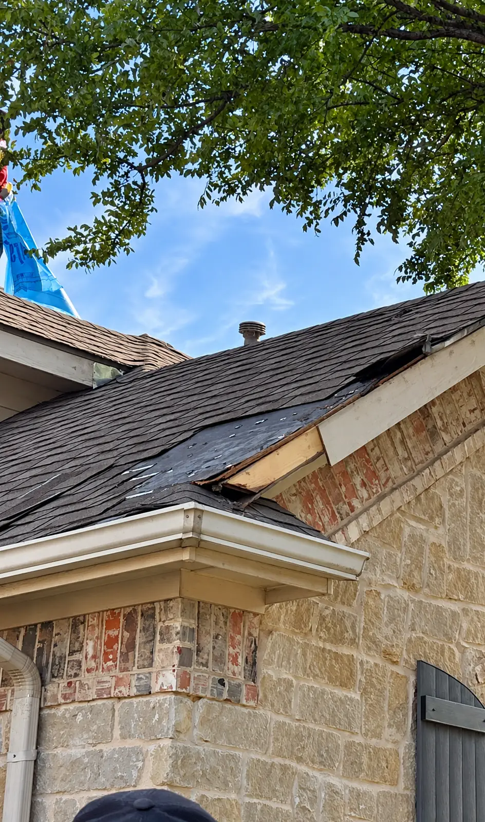 Lifted, damaged shingles along the rake edge of a brick and stone home