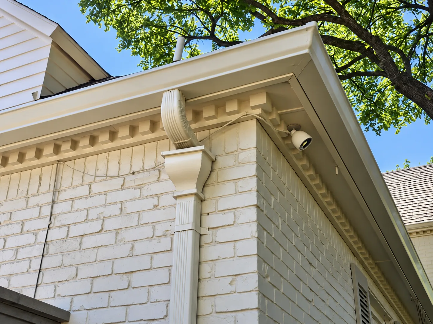 White gutter and decorative downspout on a painted brick home