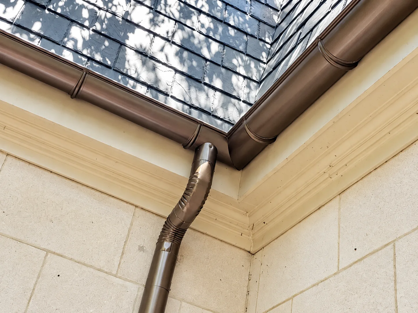 Close-up of a half-round gutter and round downspout below a slate roof
