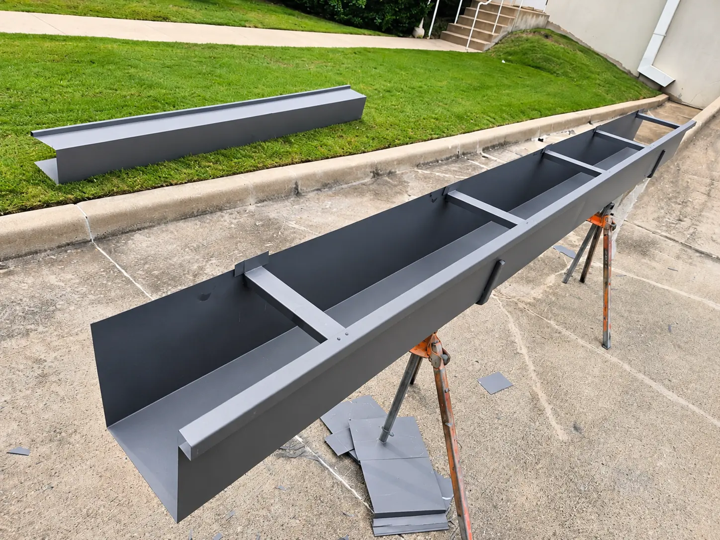 Custom dark metal box gutter section being fabricated on sawhorses