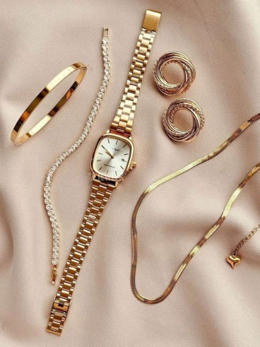 Gold watch, bangles and rings laid out on cream fabric