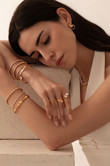 Model resting on her arm, wearing stacked gold bangles and rings