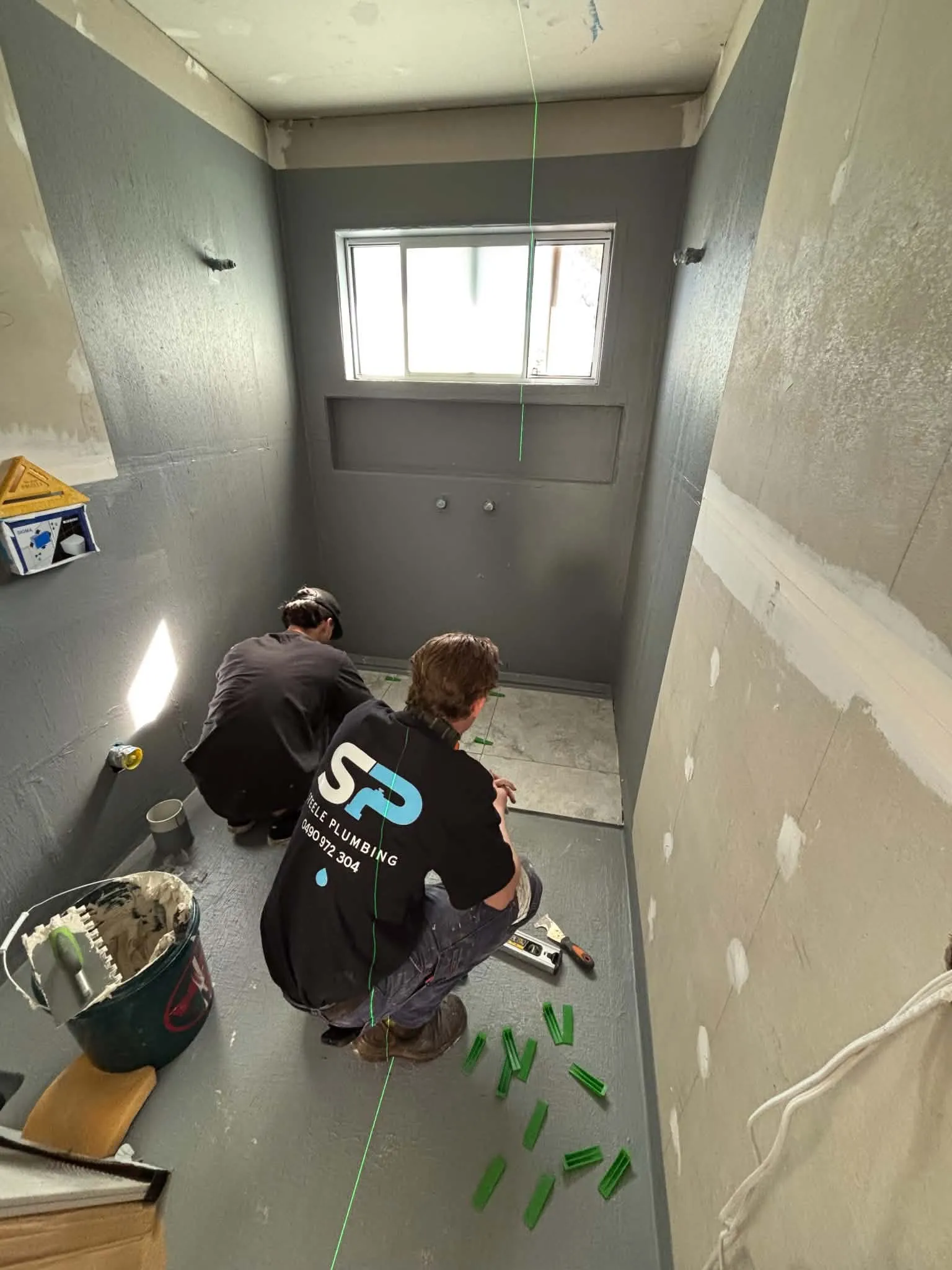 Two Steele Plumbing team members working on the floor of a bathroom renovation