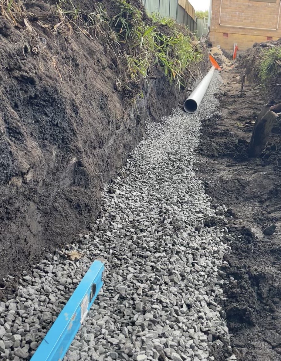 New stormwater pipe laid on a gravel bed in a trench beside a house