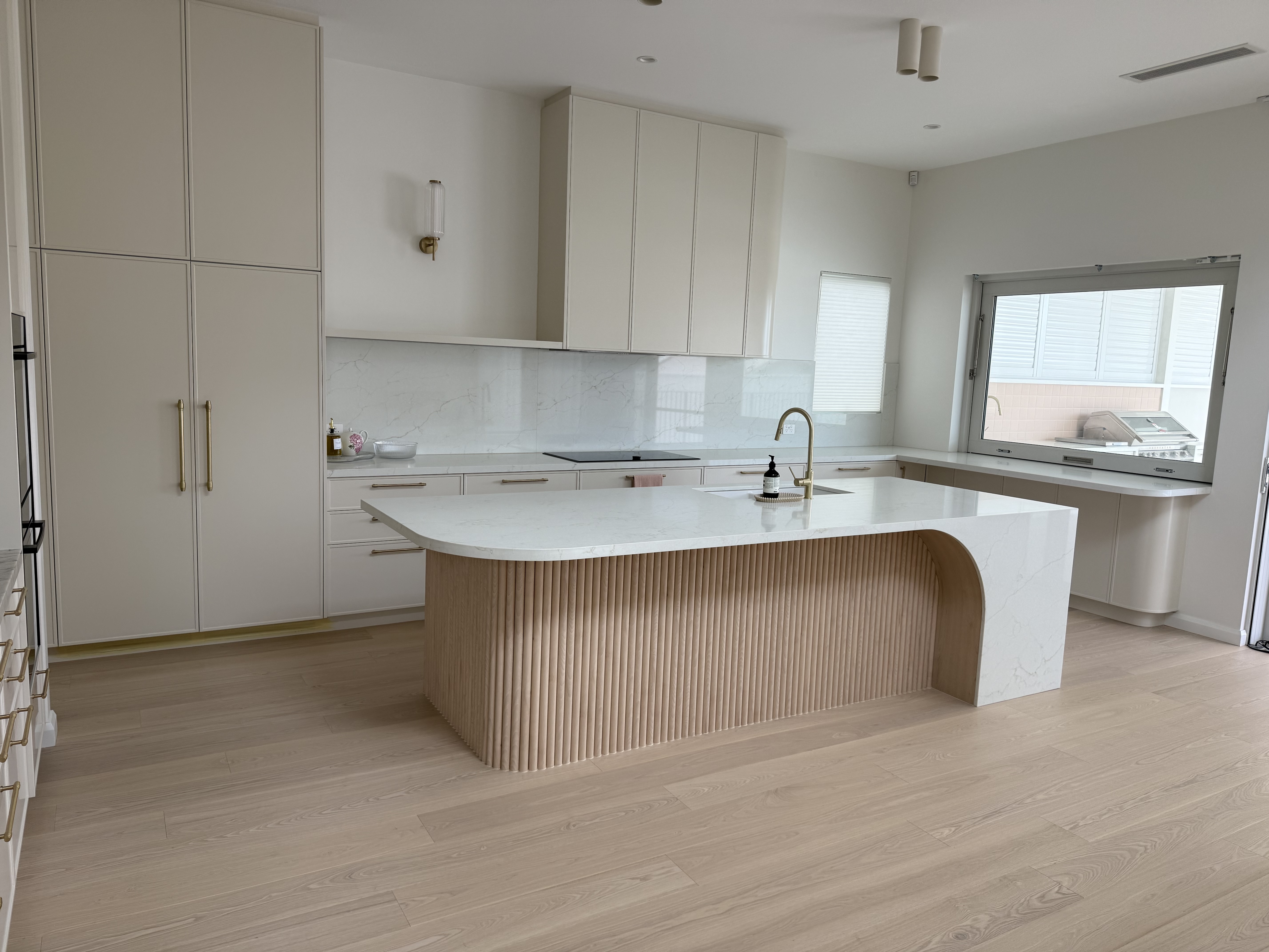 Finished kitchen renovation with a curved stone island, fluted timber base and brushed brass gooseneck tap