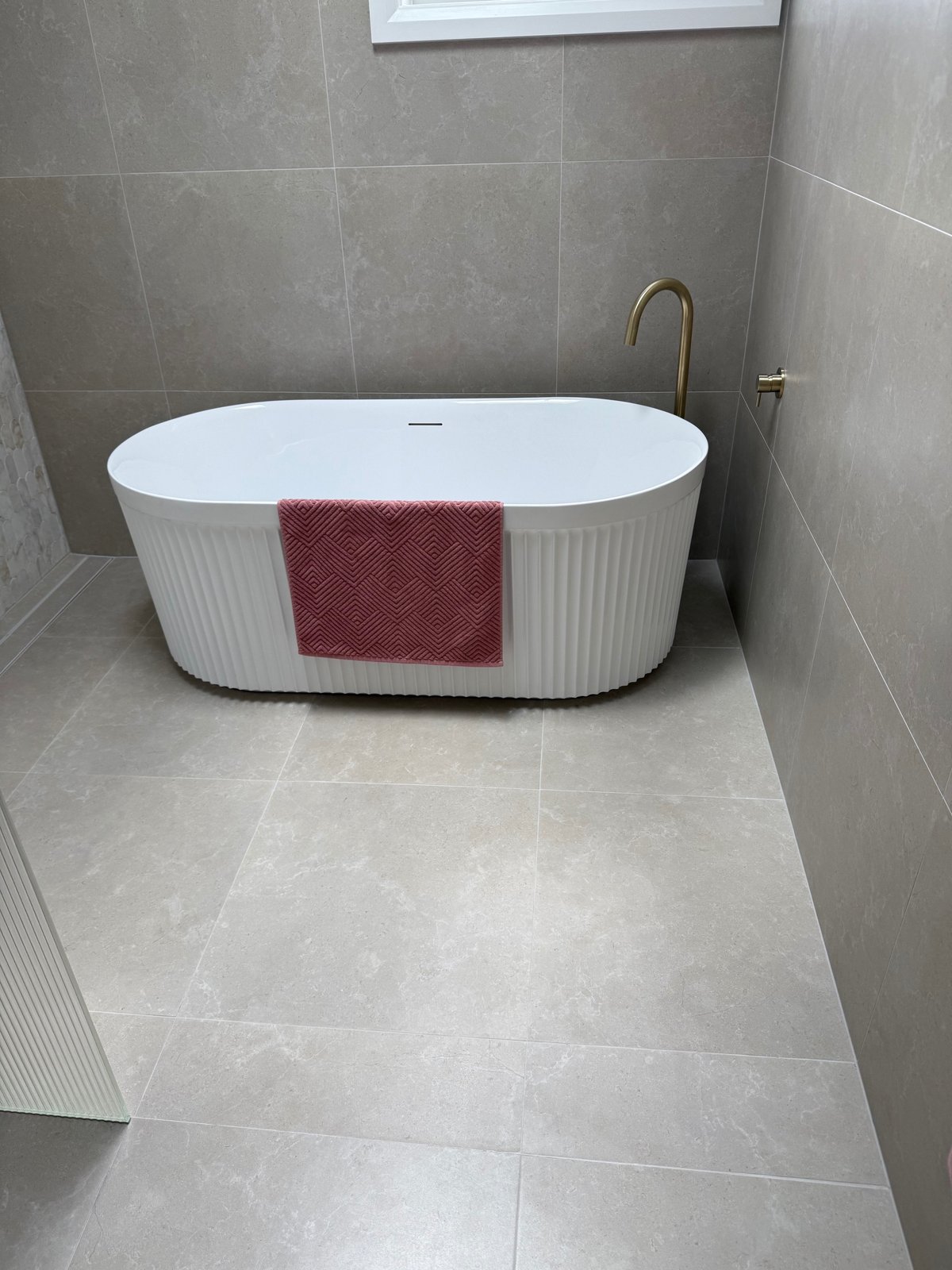 Finished bathroom with a white fluted freestanding bath, floor-mounted brushed brass bath spout and large stone-look tiles