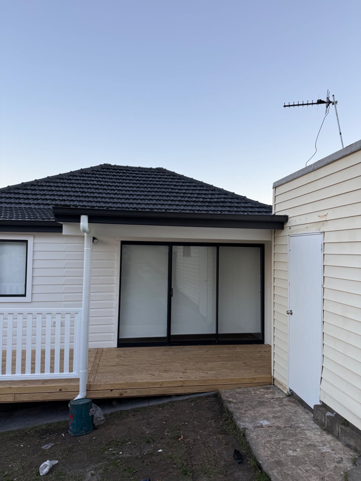 New black gutter and white downpipe installed on a rear house extension above a timber deck