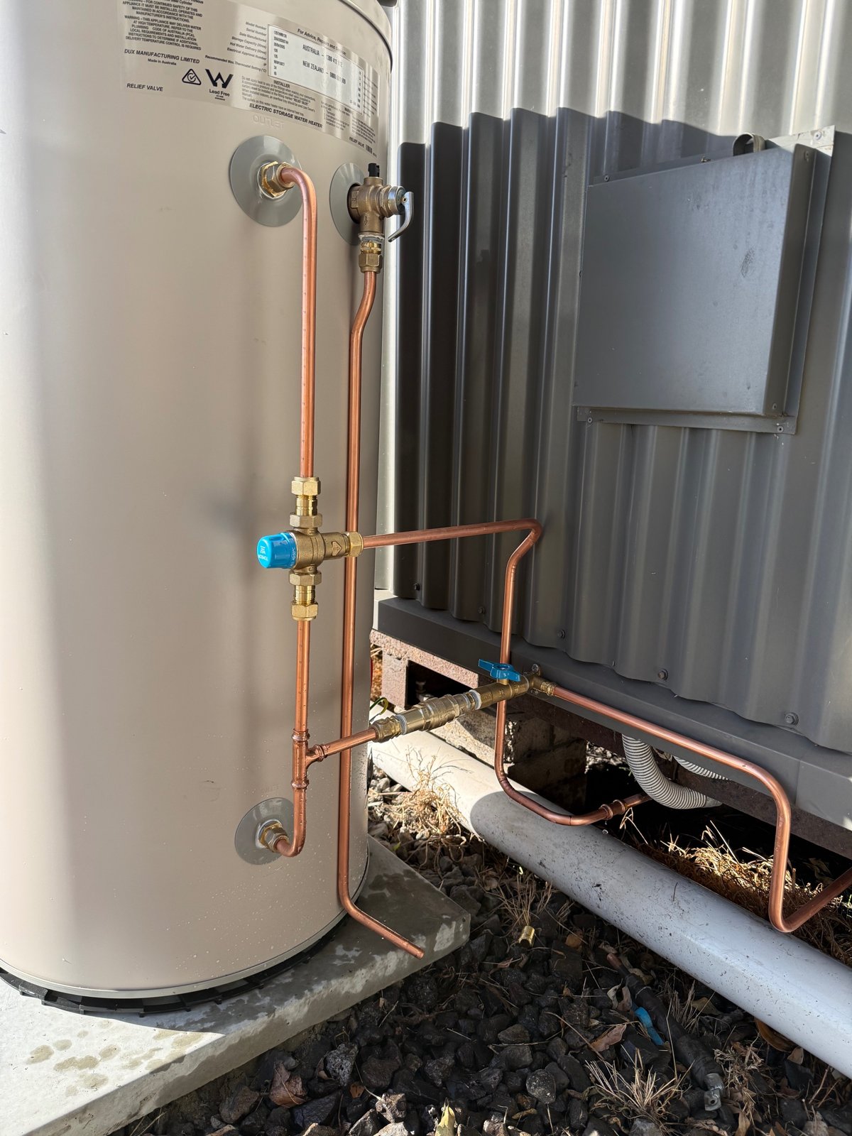 New Dux electric storage hot water system with copper pipework, tempering valve and isolation valve beside a shed extension in Towradgi