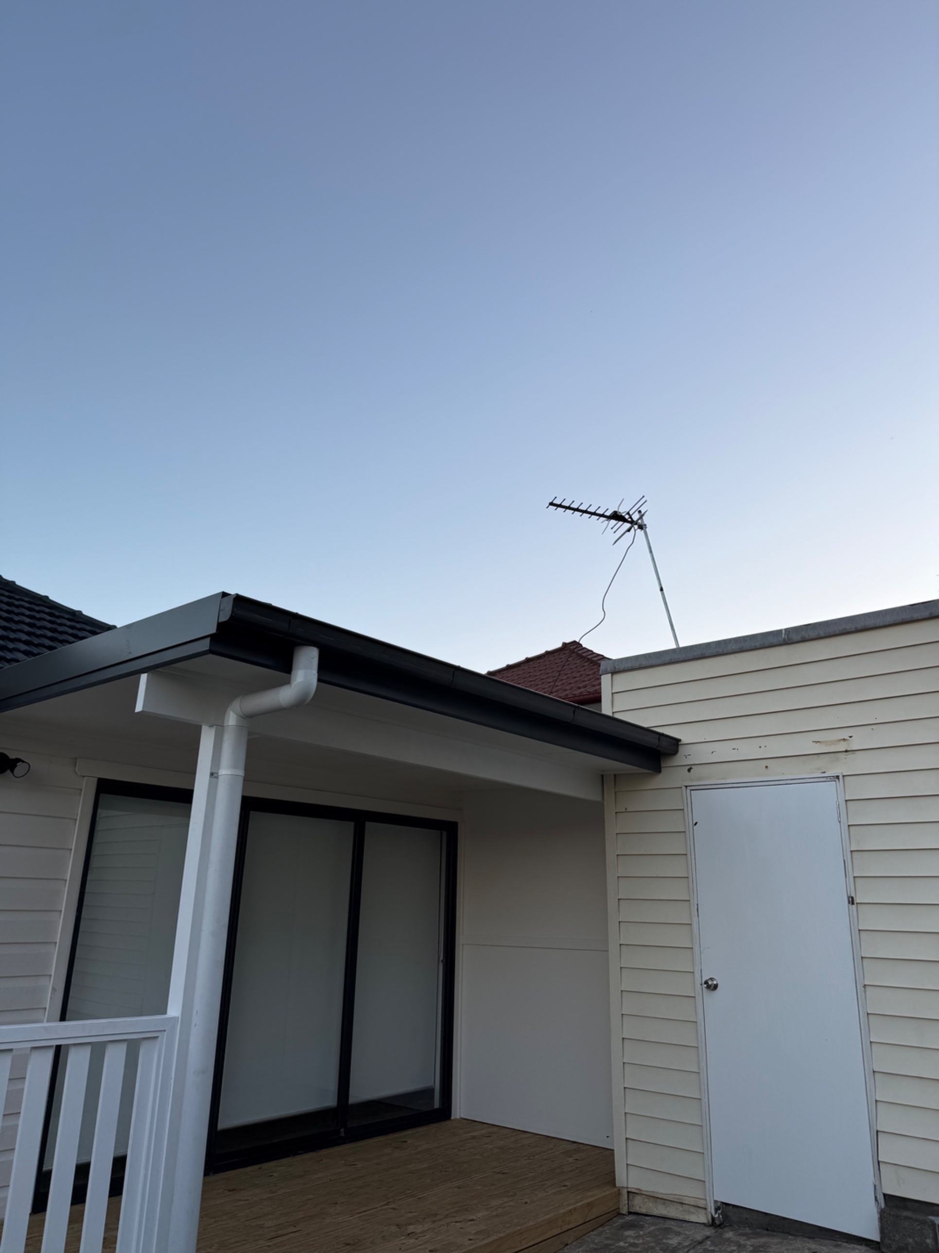 New black gutters and white downpipe on a renovated weatherboard home with a timber deck in Coniston