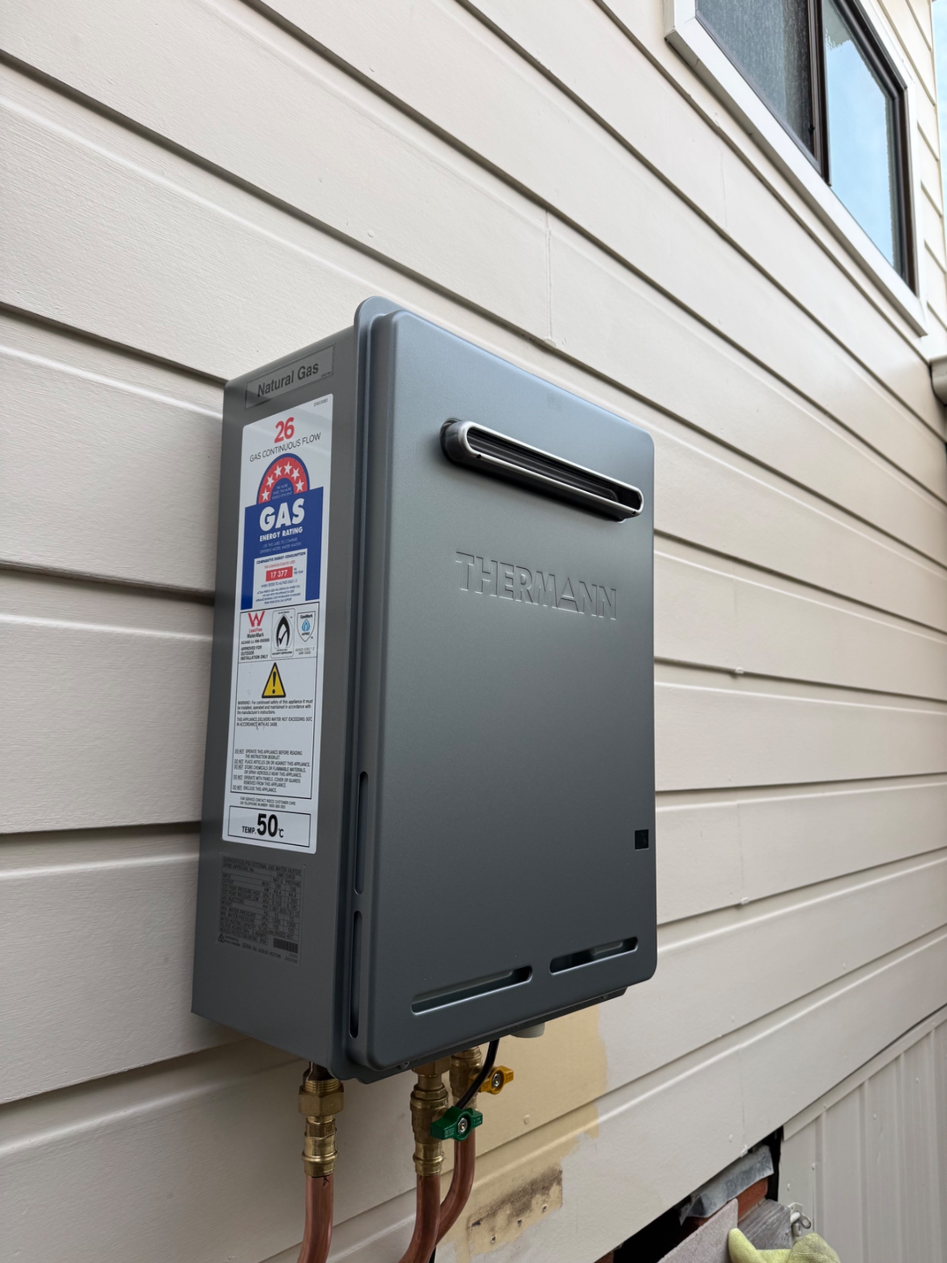New Thermann 26 natural gas continuous flow hot water system with copper connections on a weatherboard wall in Bellambi