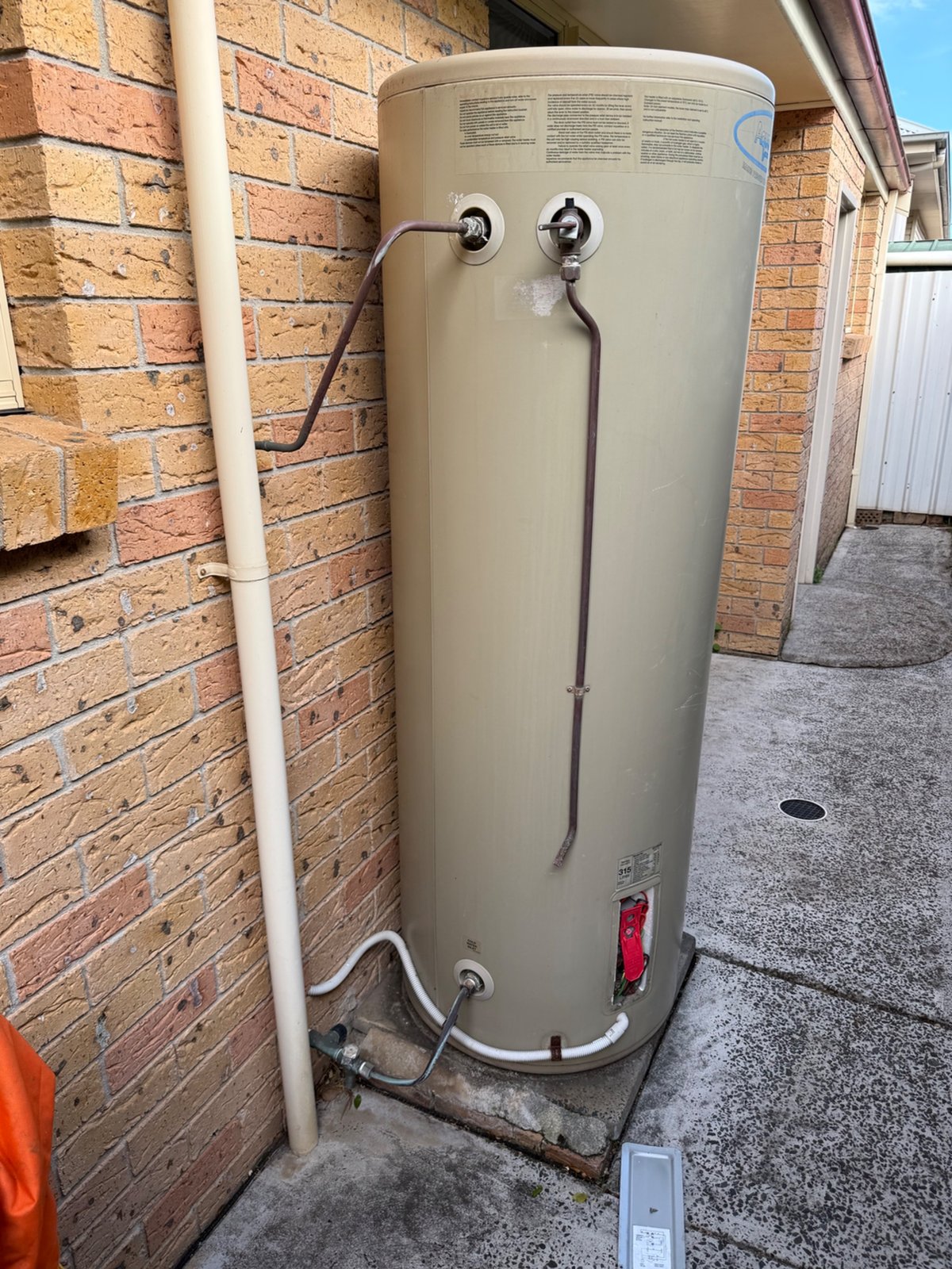 Old Aquamax 315 litre electric storage hot water system with tired pipework beside a brick wall