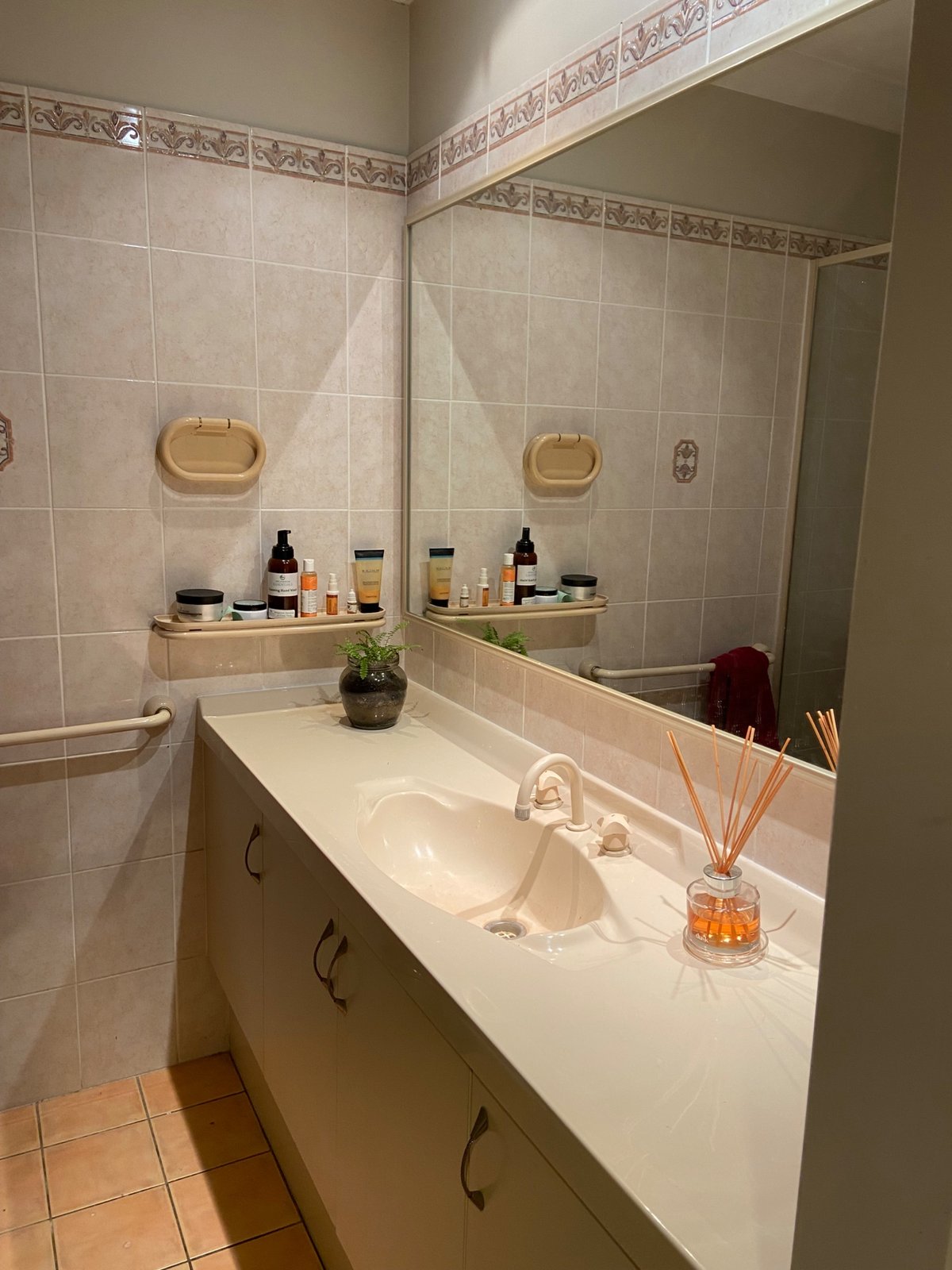 Dated bathroom with a beige moulded vanity basin, cream tapware and pink border tiles