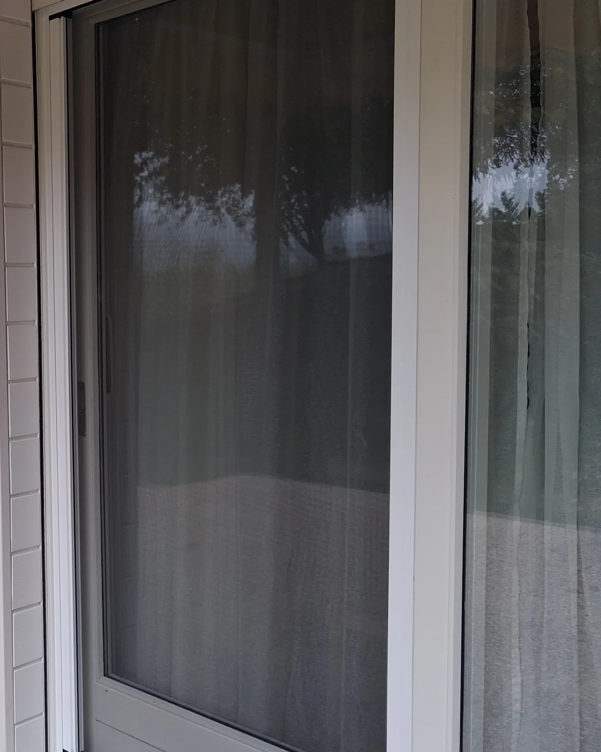 Porte-fenêtre sur une terrasse de Vétraz-Monthoux fermée par une moustiquaire latérale enroulable : la toile grise couvre tout le vitrage, le voilage se devine au travers.