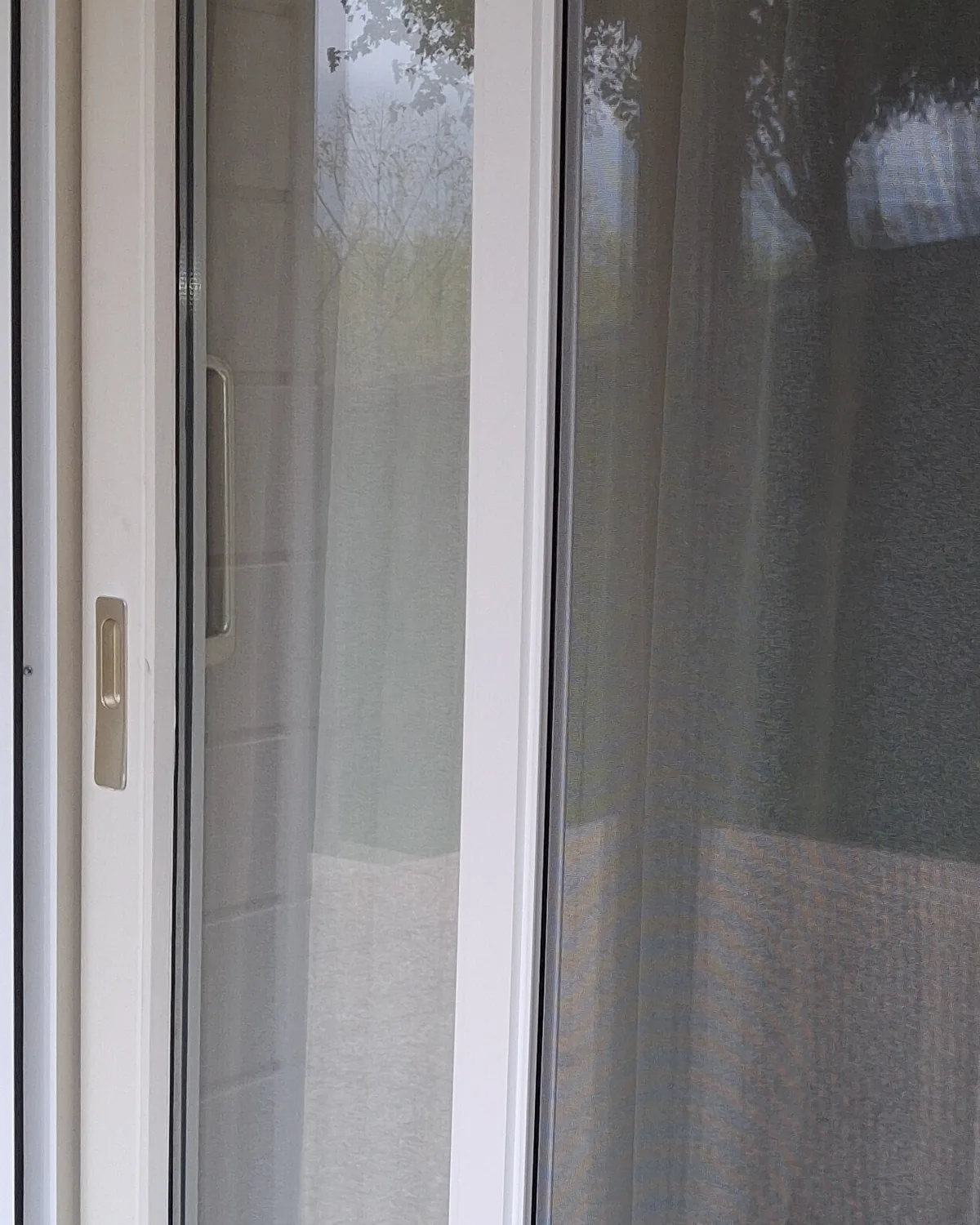 Porte-fenêtre blanche de Vétraz-Monthoux en gros plan : la barre de tirage de la moustiquaire latérale enroulable et sa poignée, la toile tirée devant le vitrage.